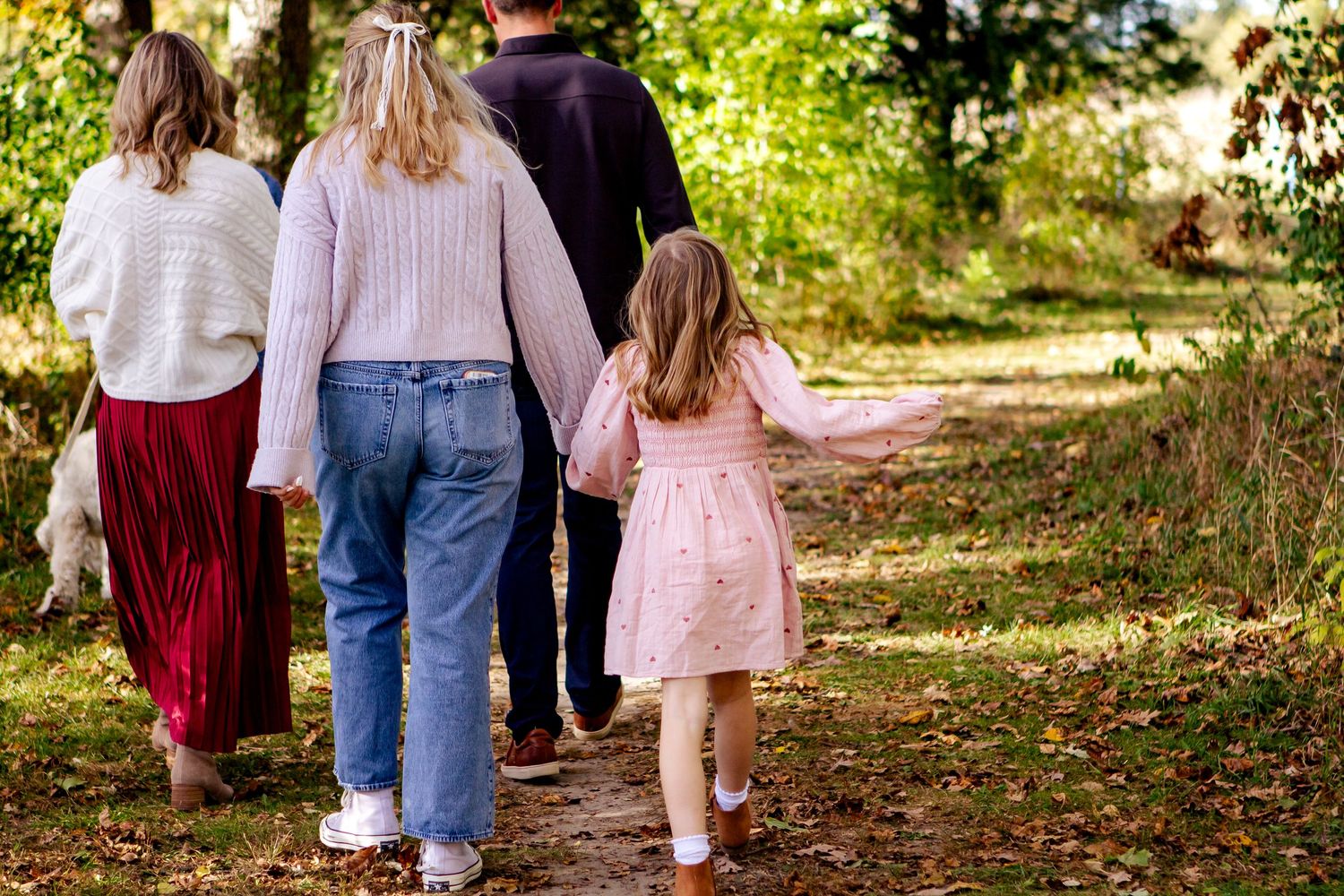 Family walking together on a leaf-covered autumn path in casual clothing.
