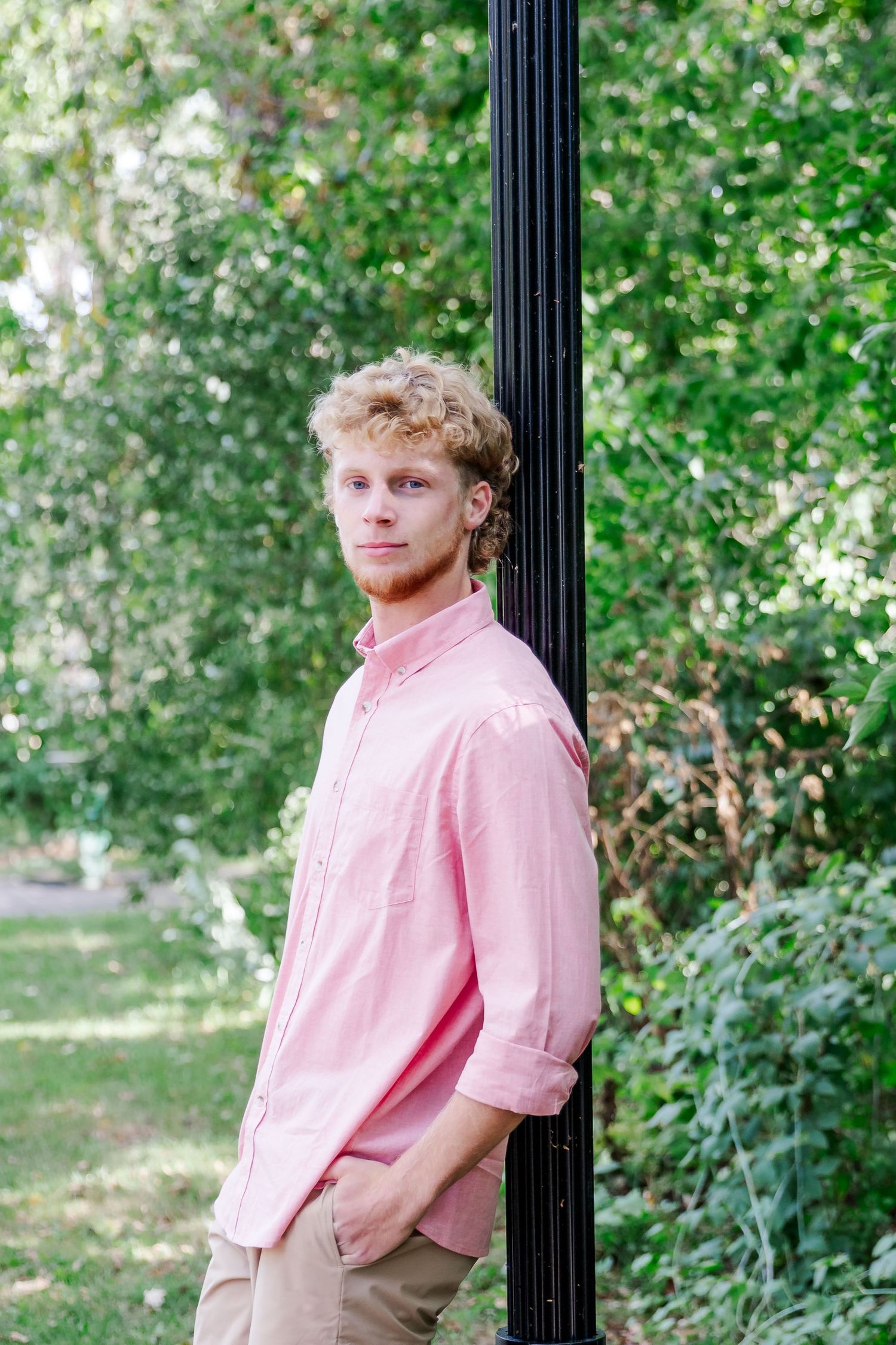 Person in pink button-down shirt leans against black post in outdoor garden setting during a Michigan senior session
