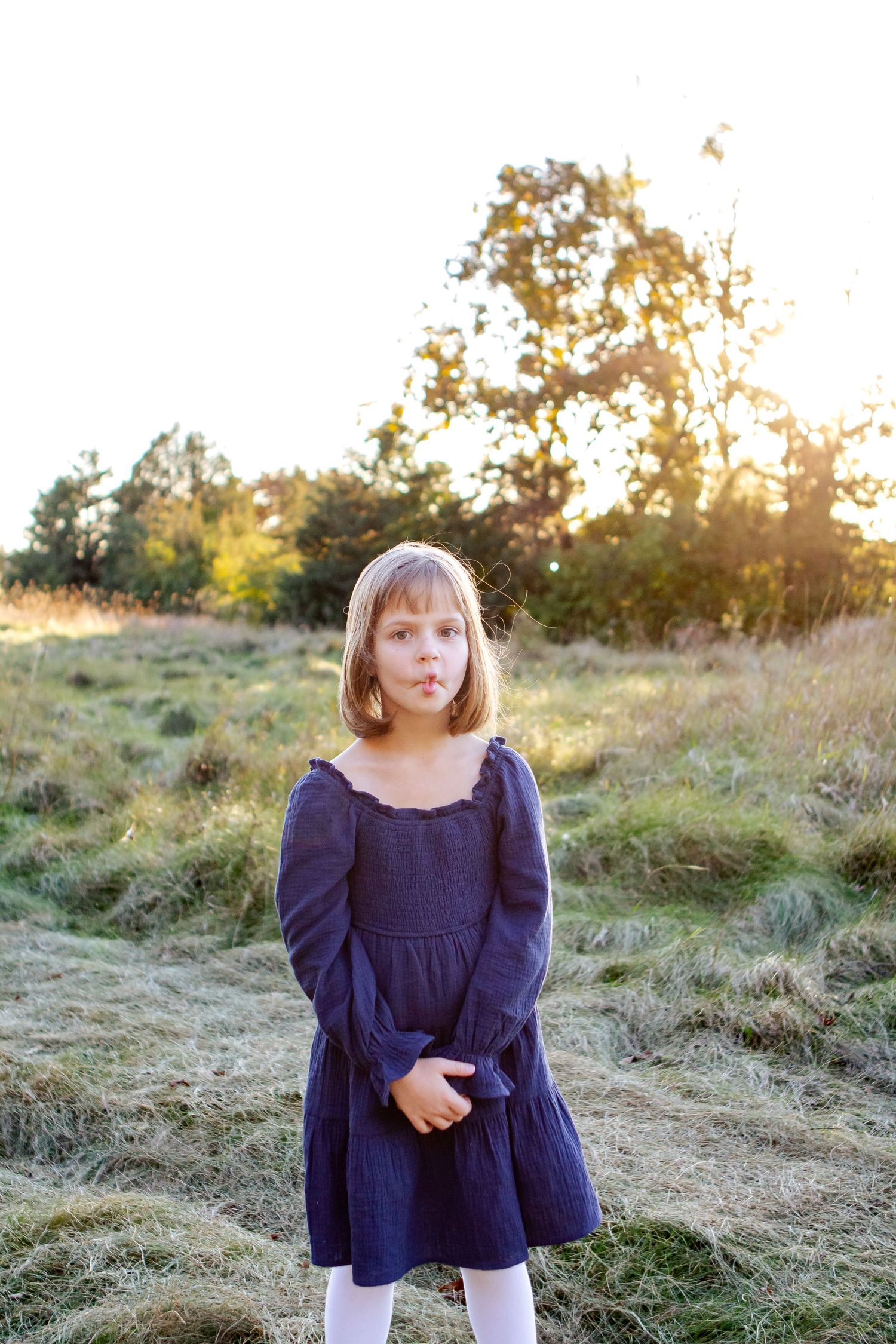 A child in a navy blue dress stands in a golden field at sunset during a photo session at an Oconomowoc family session