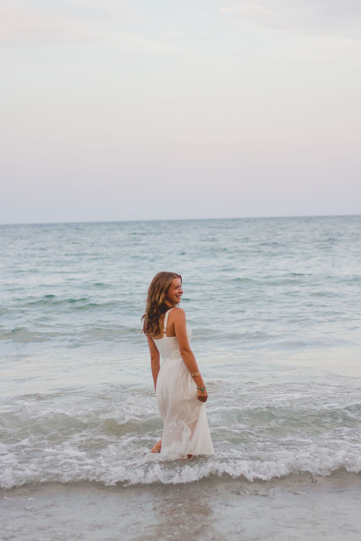 Someone in a white sundress plays in the ocean waves during a beach photoshoot.