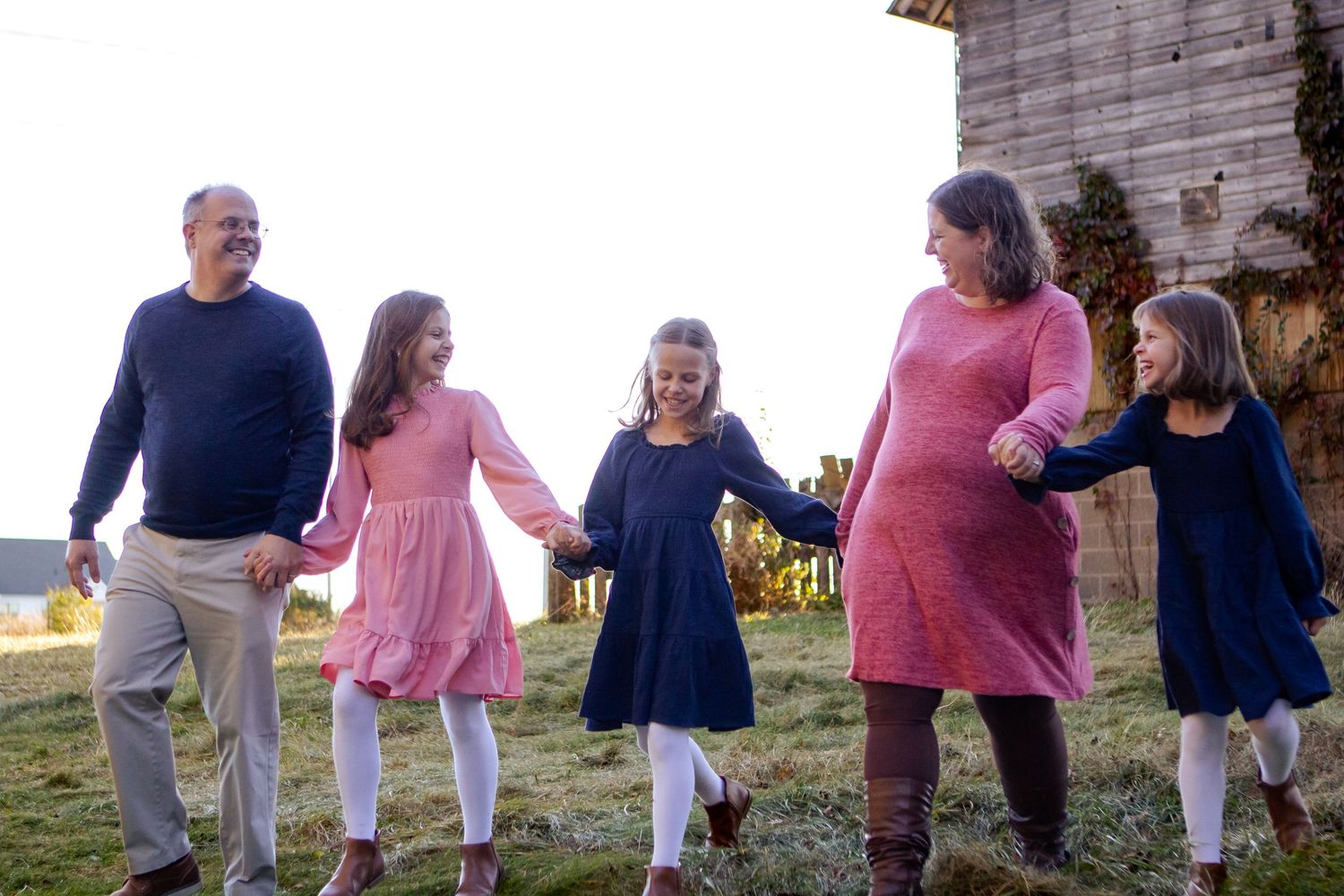 A family group holds hands while walking together outdoors at sunset in coordinated pink and navy outfits at an Oconomowoc family session