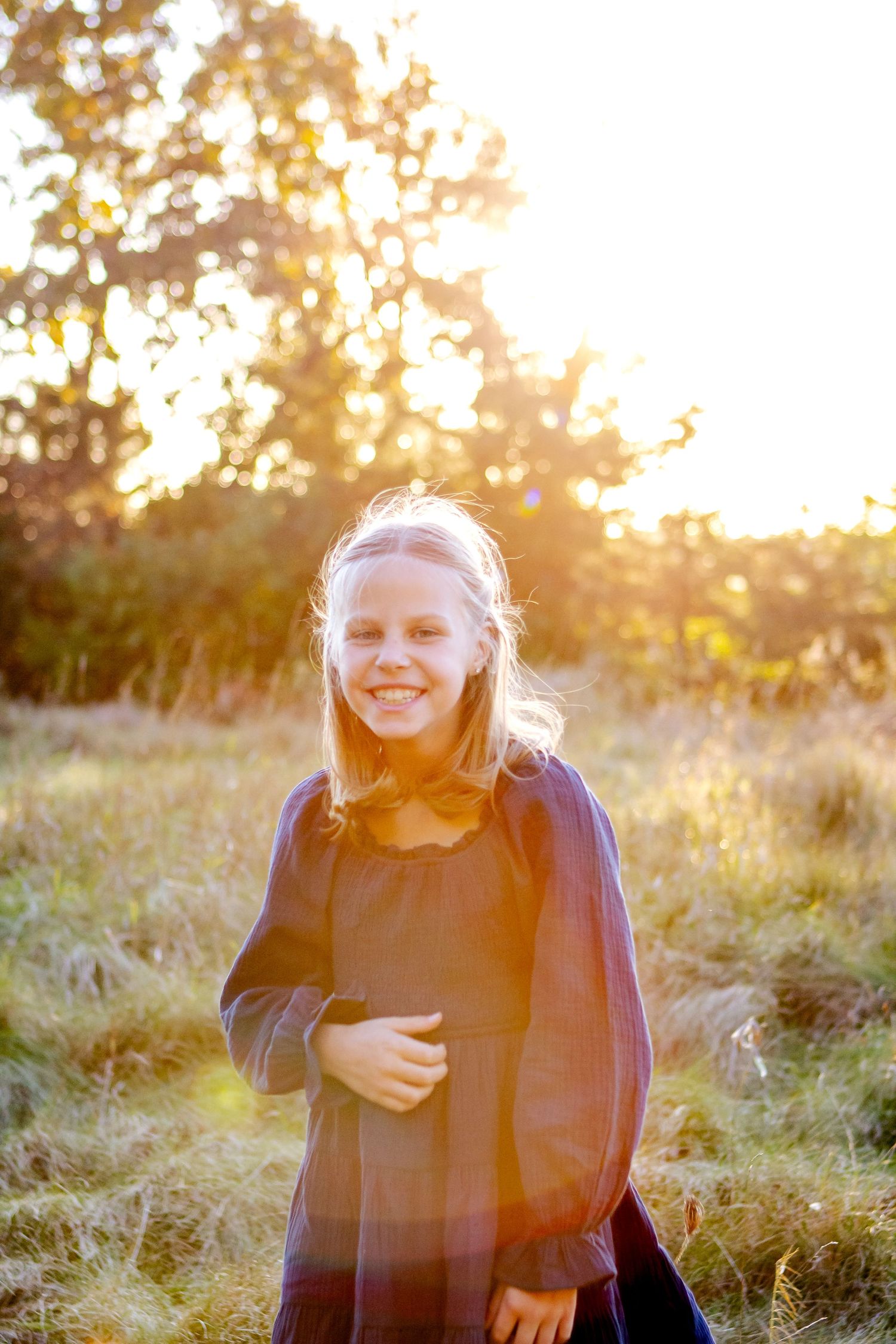 A girl laughs joyfully in a field during golden hour sunset with sunlight creating a warm glowing atmosphere at an Oconomowoc family session