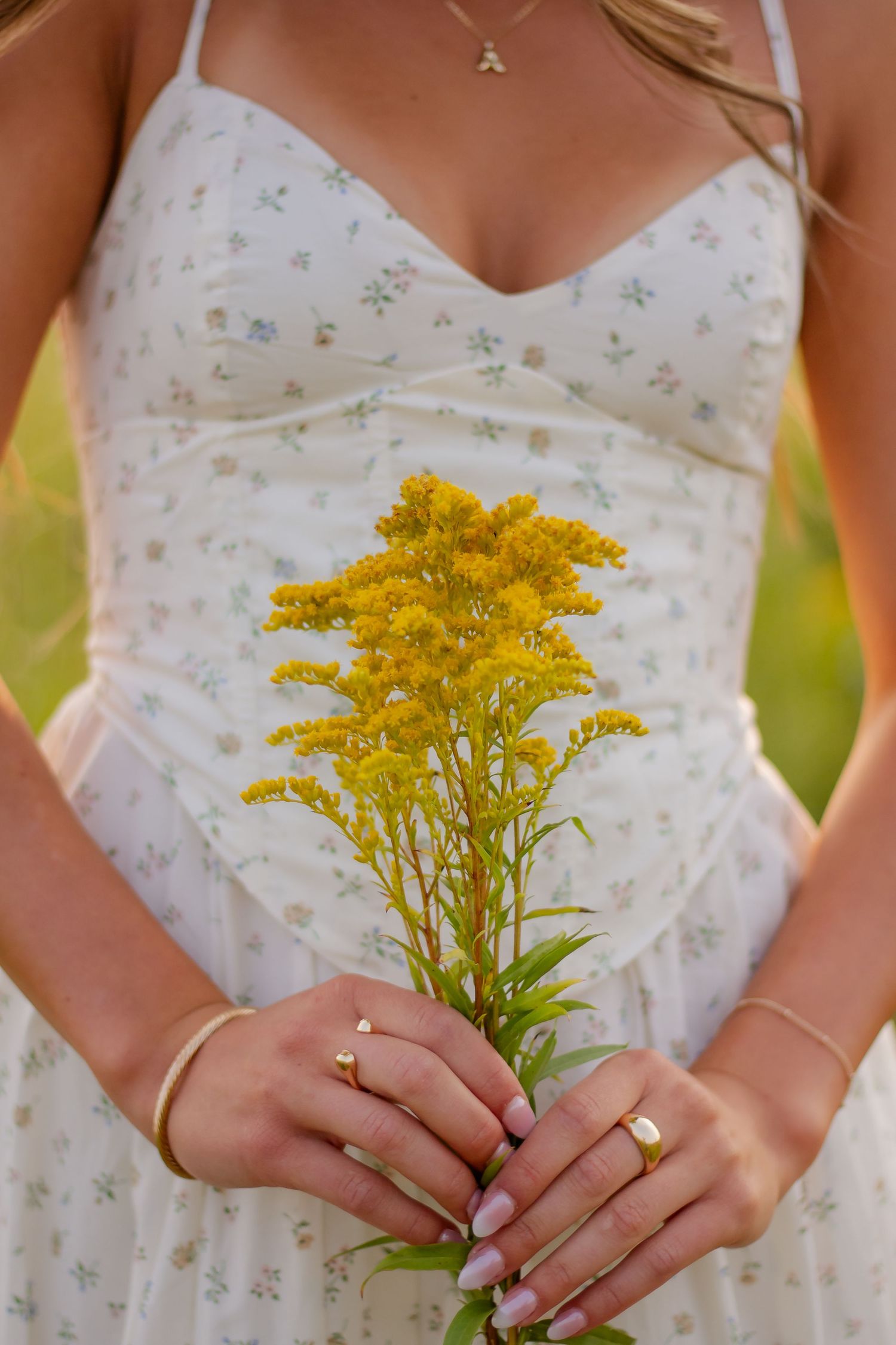 Close-up shot of hands holding yellow wildflowers against a white floral dress.
