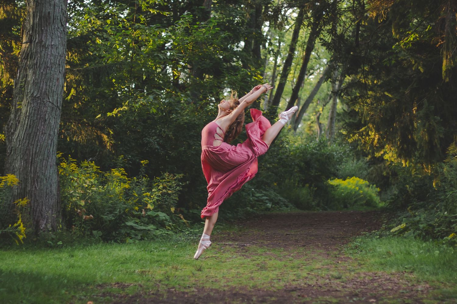 Dancer executing dynamic jump pose against wooded background.