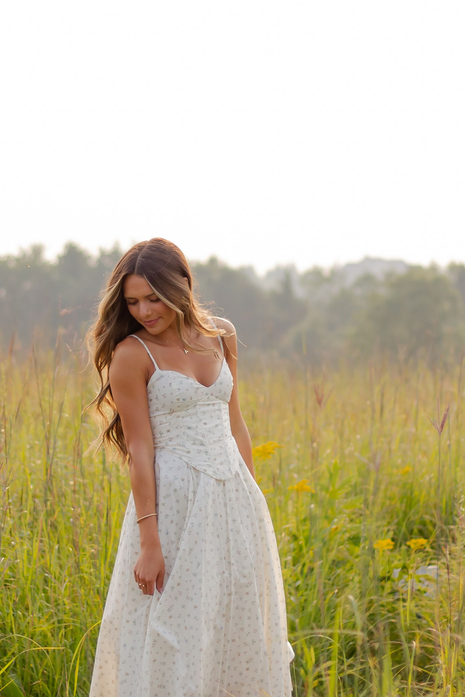 Woman in white sundress walking through tall grass in a summer meadow.