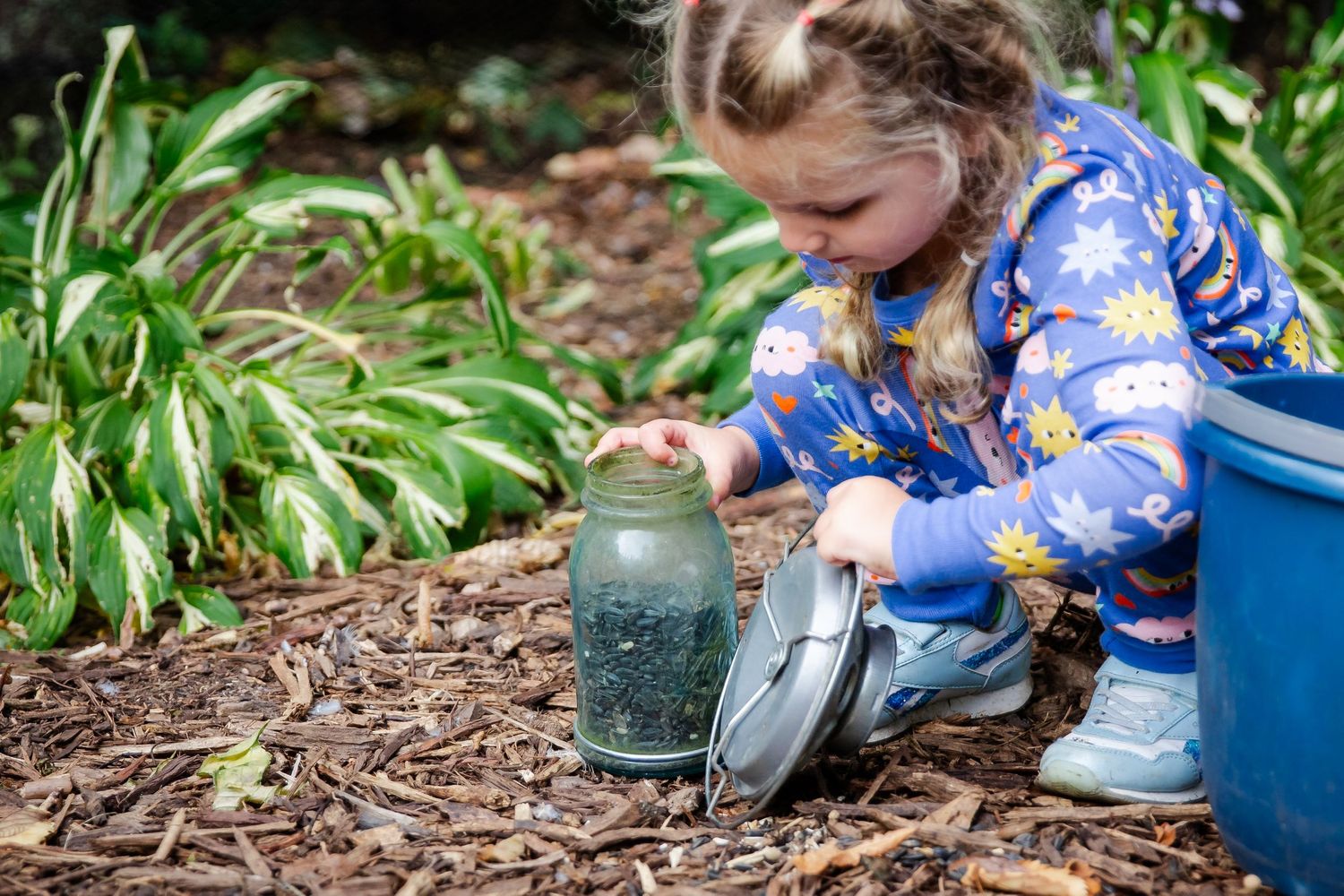 A person in blue floral clothing kneels down to examine mason jars in a garden setting at Delafield home session