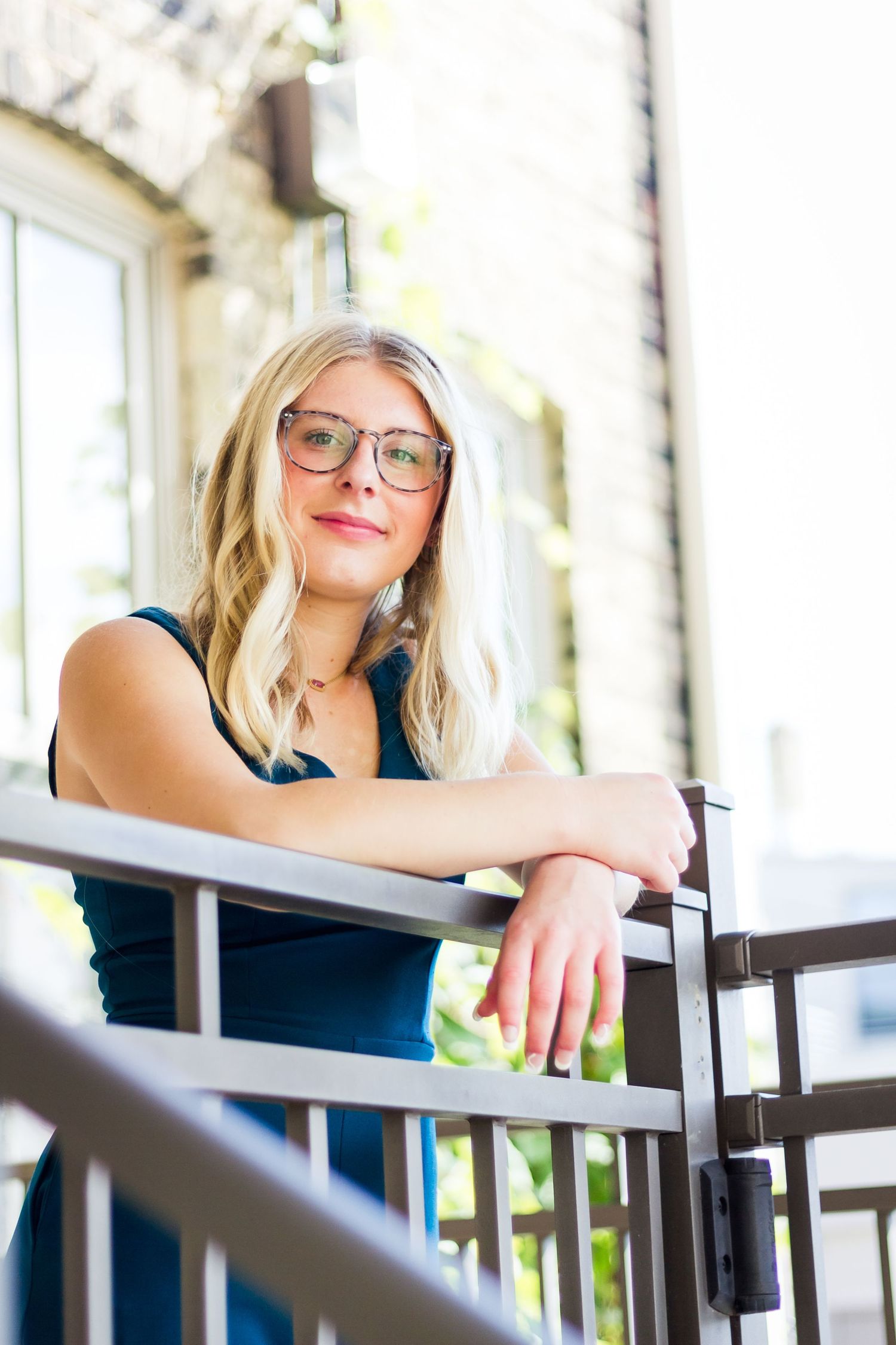 Portrait of someone in glasses leaning on a railing in an urban setting with soft natural lighting.