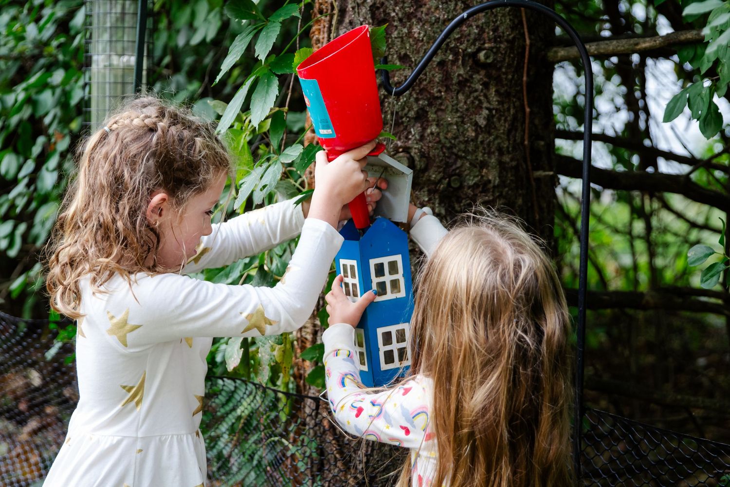 A person in a white sweater interacts with a decorative red and blue birdhouse mounted on a tree trunk at Delafield home session