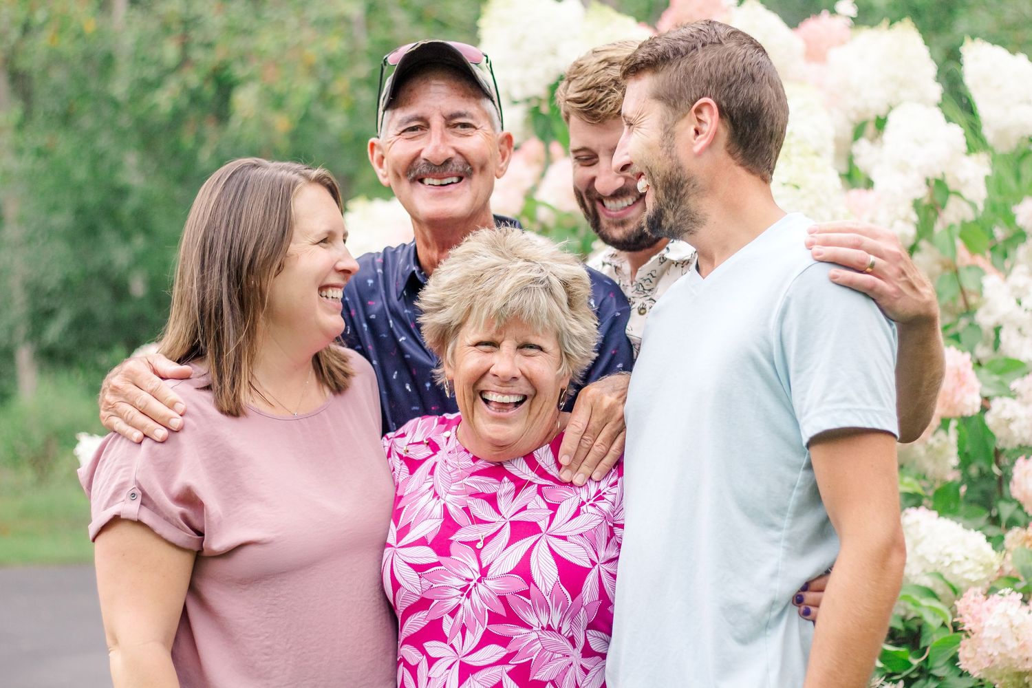 A group of people share joyful moments together in a sunny outdoor setting with green foliage in the background at Delafield home session