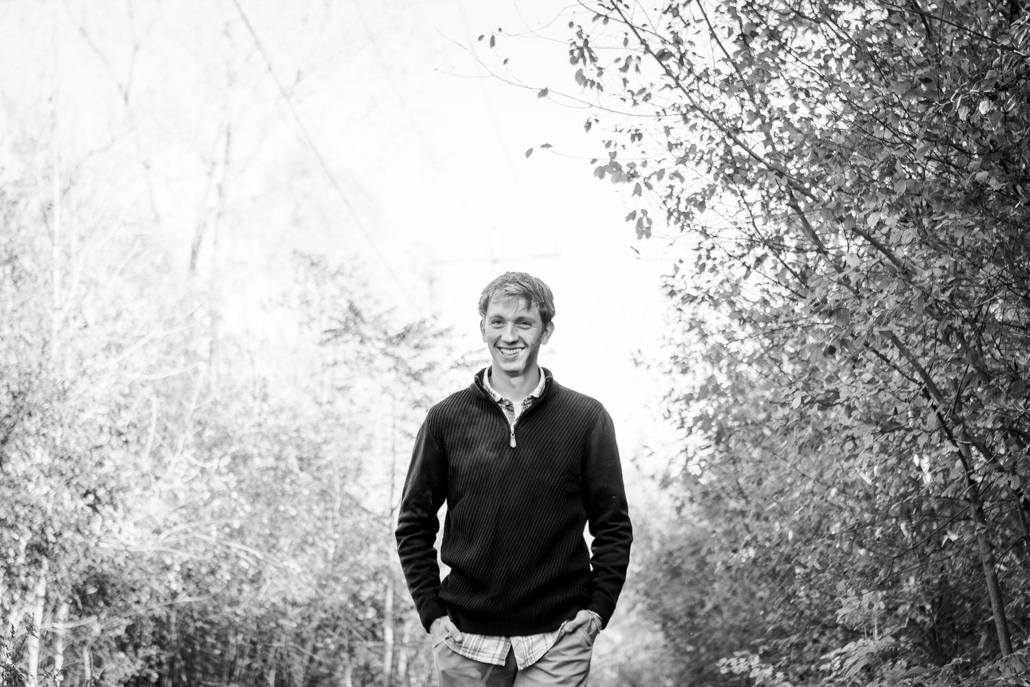 Black and white outdoor portrait of someone in a quarter-zip sweater standing among trees on a bright day during his Hartland senior session