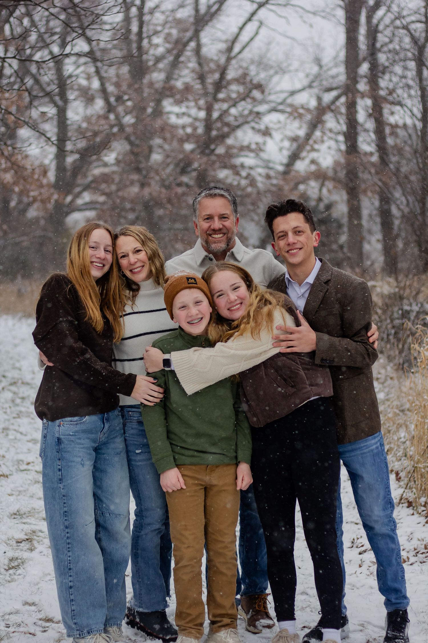 A family group hugging and smiling together on a snowy winter day in the woods.