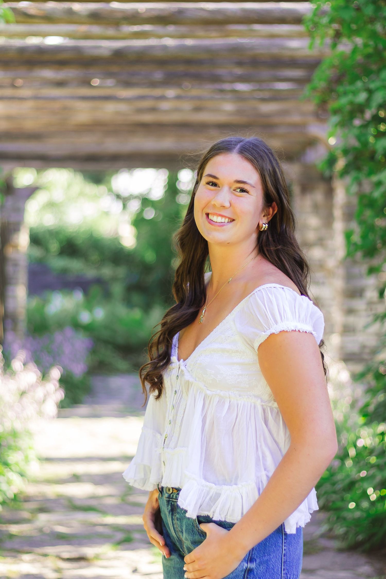 A summer photoshoot under a wooden pergola surrounded by garden greenery.