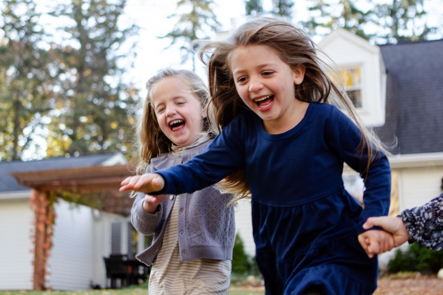 Two children running and laughing together outside a suburban home.