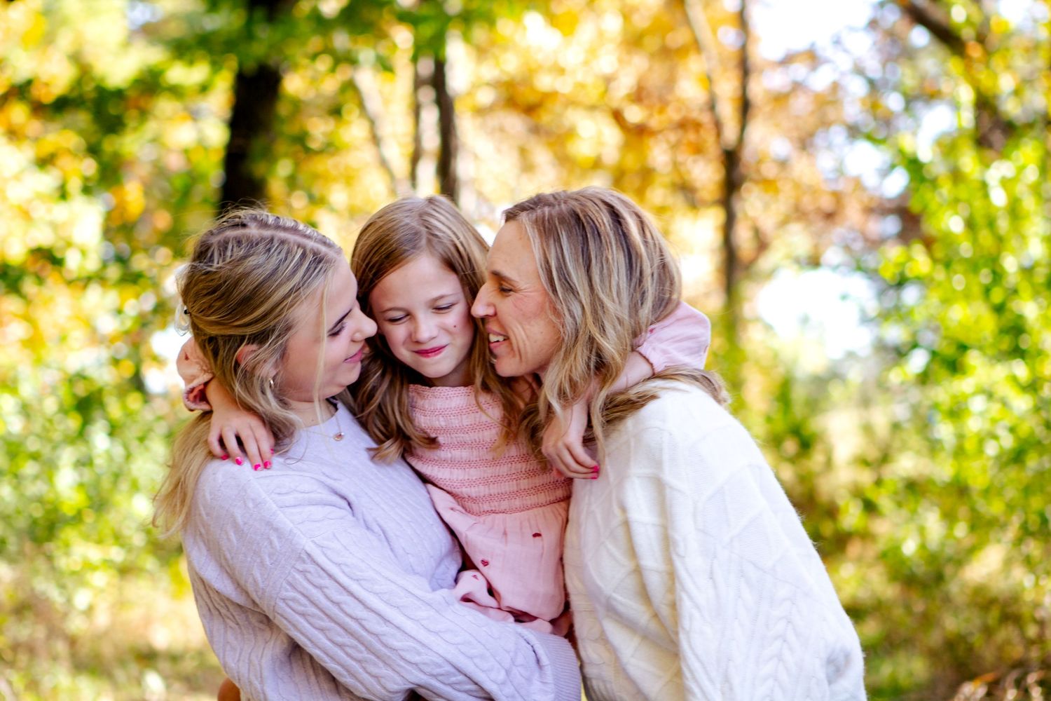 A loving family shares tender moments together in a sunny autumn setting with golden foliage in the background at an Oconomowoc family sessi