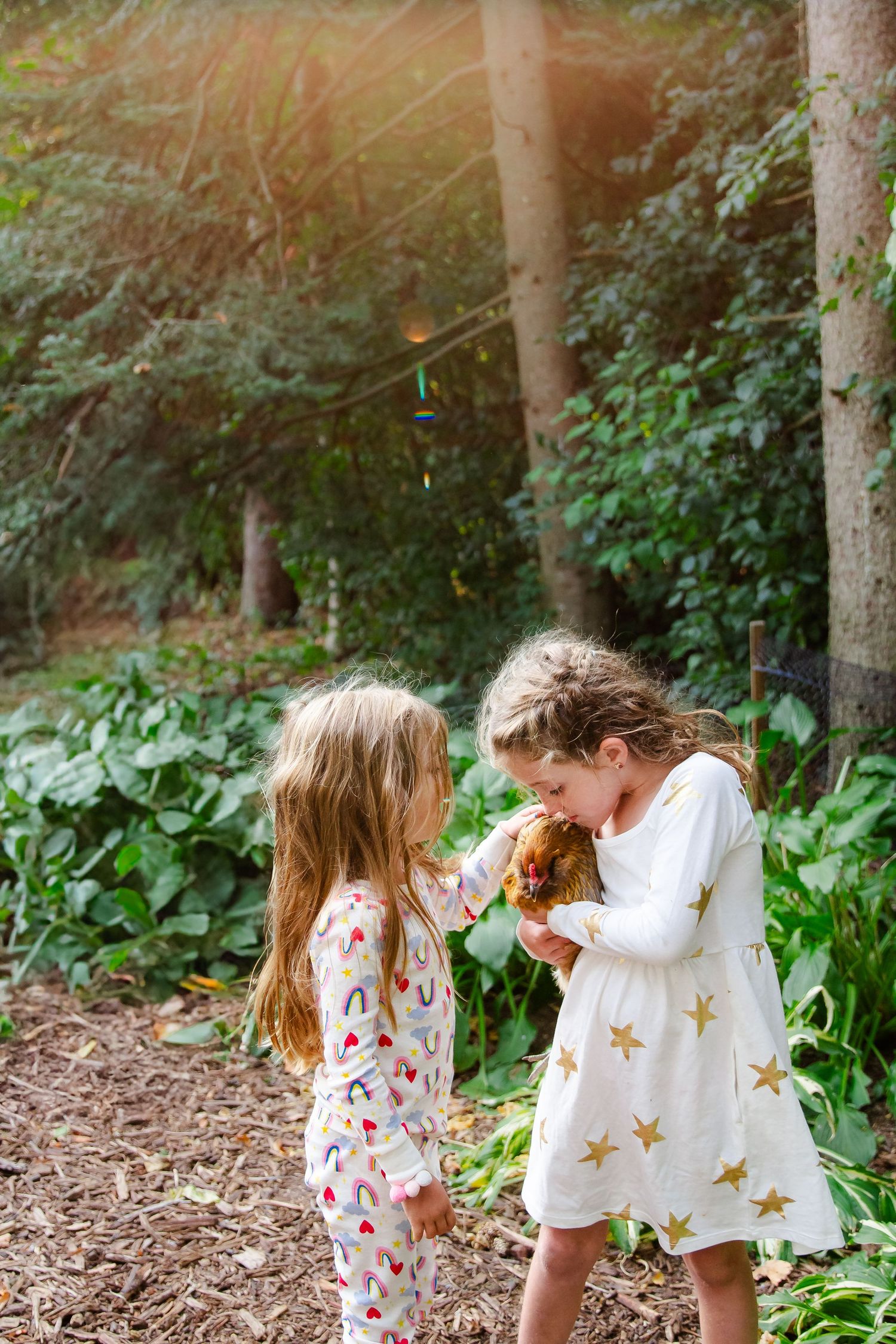 Two children in white and floral dresses play together in a wooded area with dappled sunlight at Delafield home session