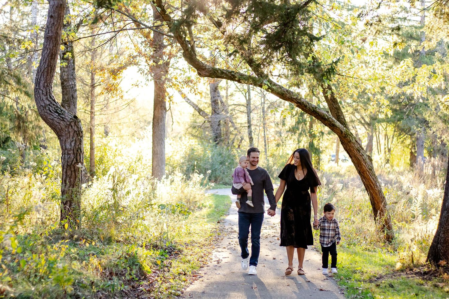 A family walking together on a sunlit path through a wooded park.