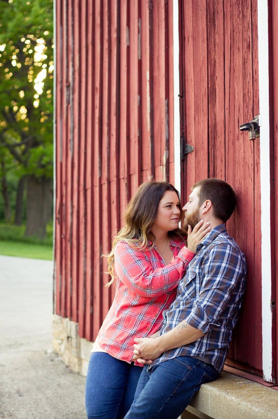 A couple in matching blue jeans share an intimate moment against a rustic red barn wall.