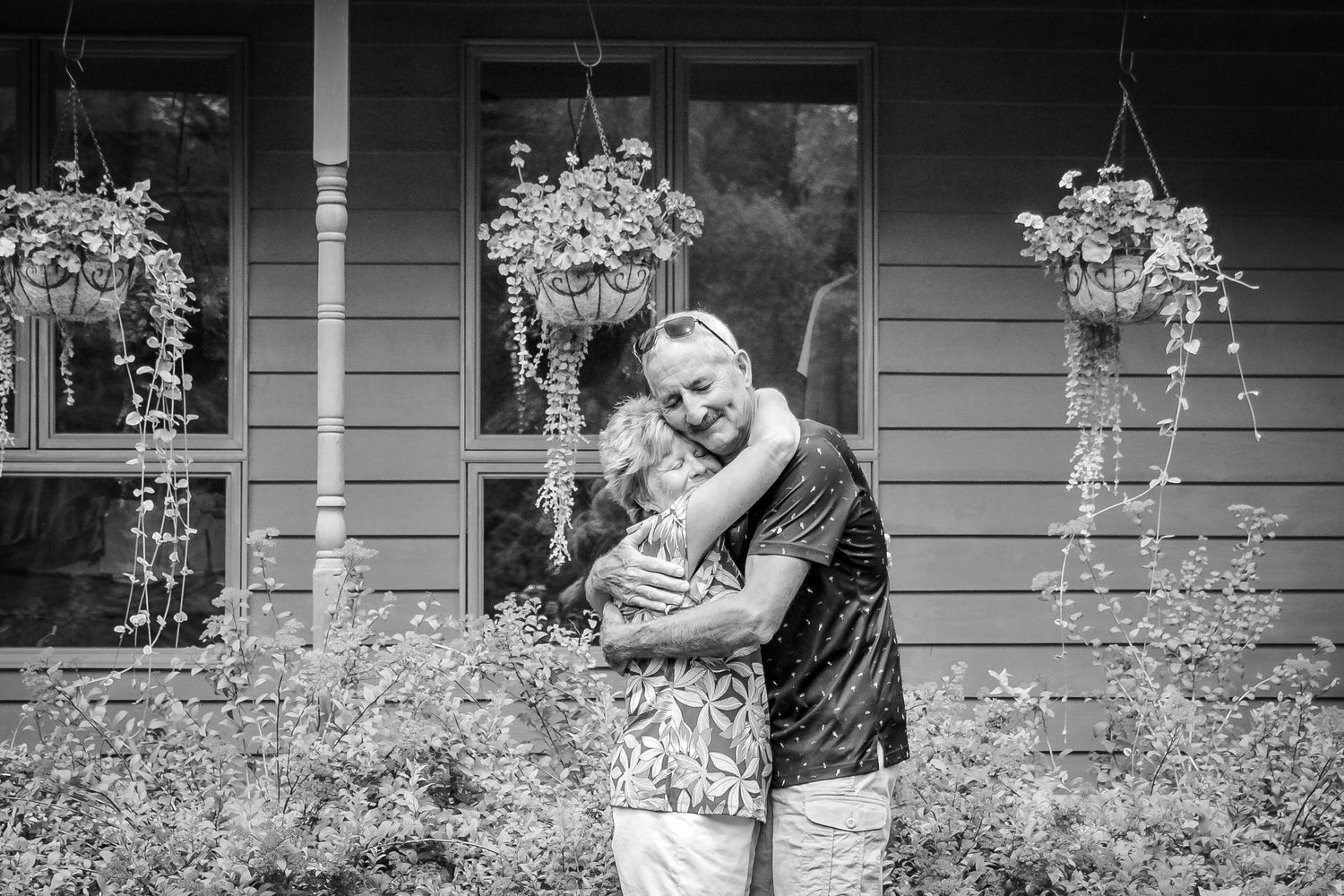 A romantic black and white photo sequence shows a couple embracing in front of a house with flowering bushes at Delafield home session