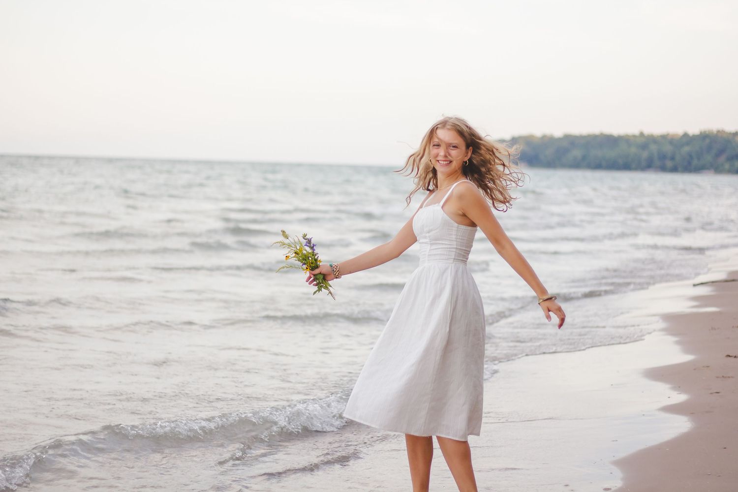 A flowing white dress catches the breeze along a scenic beach shoreline.