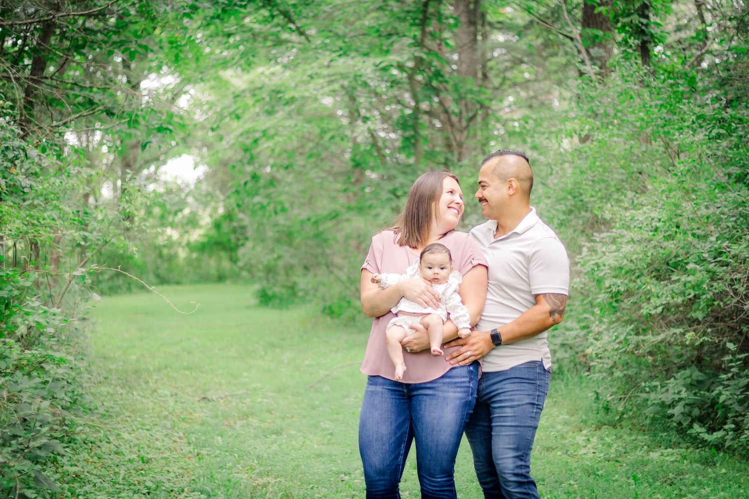 A family shares tender moments together in a lush green outdoor setting during a summer photoshoot at Delafield home session