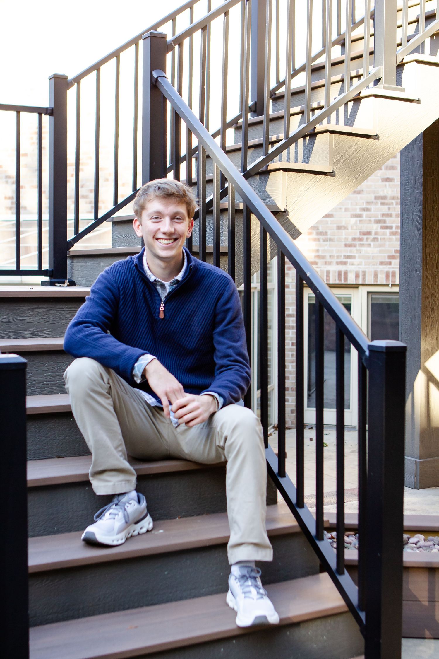A person in a navy blue sweater and khaki pants sits casually on outdoor wooden stairs with black metal railings during his Hartland session