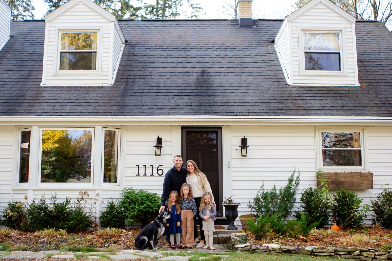 Family poses with dog outside of home during fall photo session in Delafield