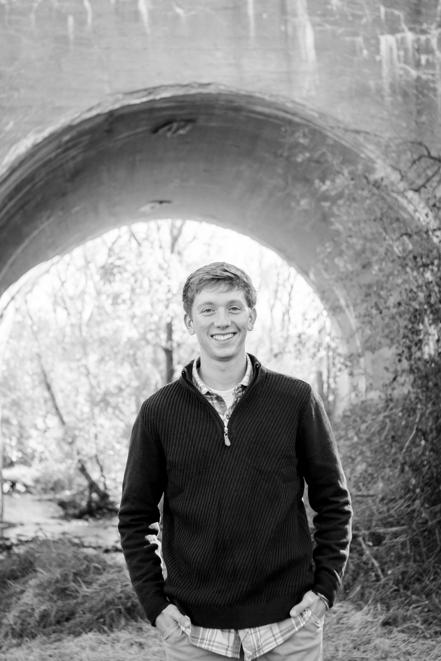 Black and white photo series showing a boy in a dark sweater posing outdoors against a stone archway background during his Hartland photos