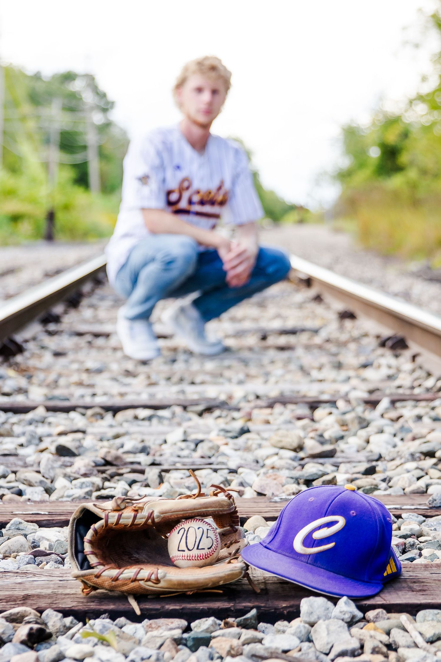 Baseball glove and cap rest on railroad tracks while someone sits blurred in the background during a Michigan senior session