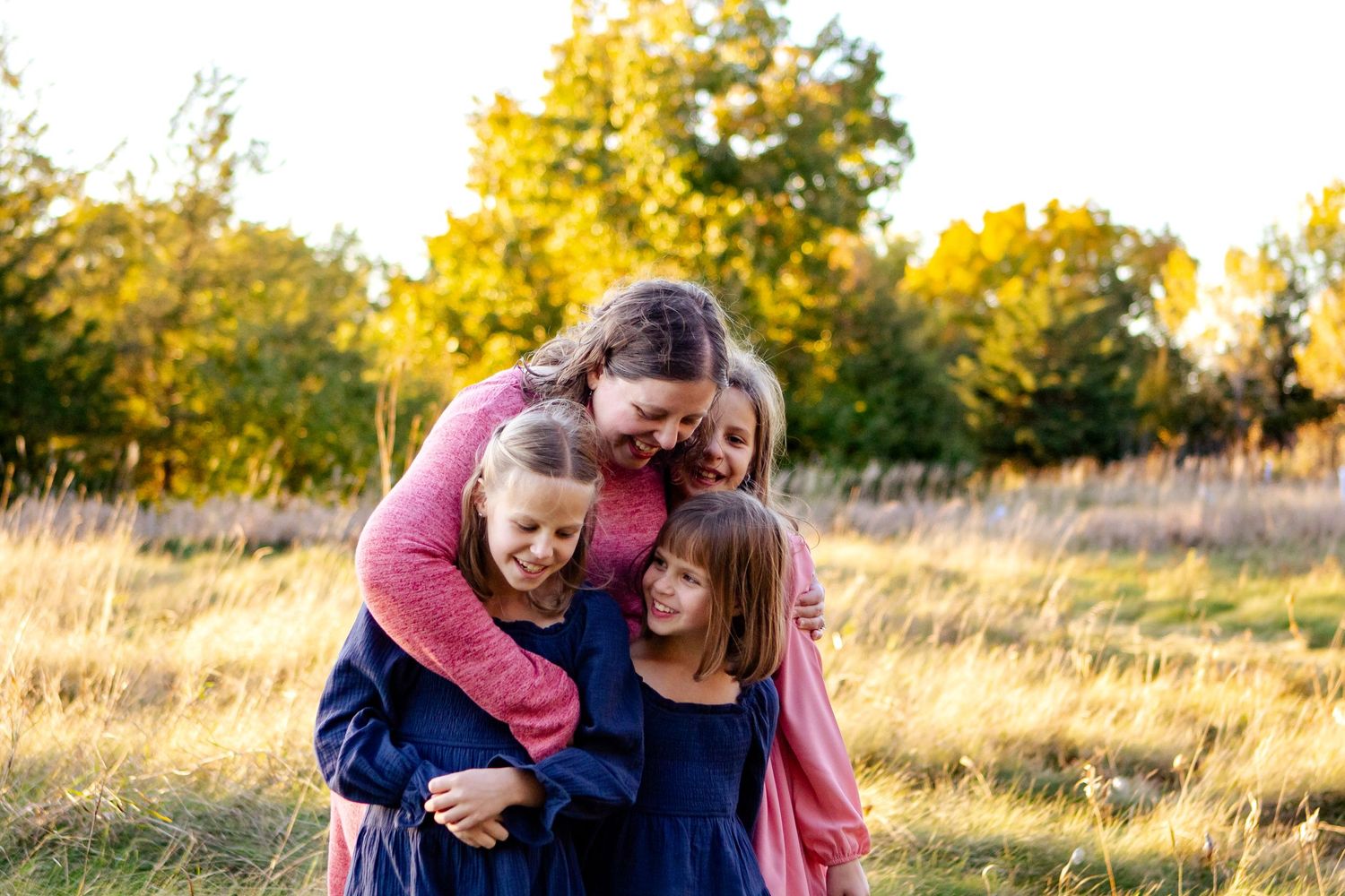 A family shares a tender moment together in a sunlit field during golden hour at an Oconomowoc family session