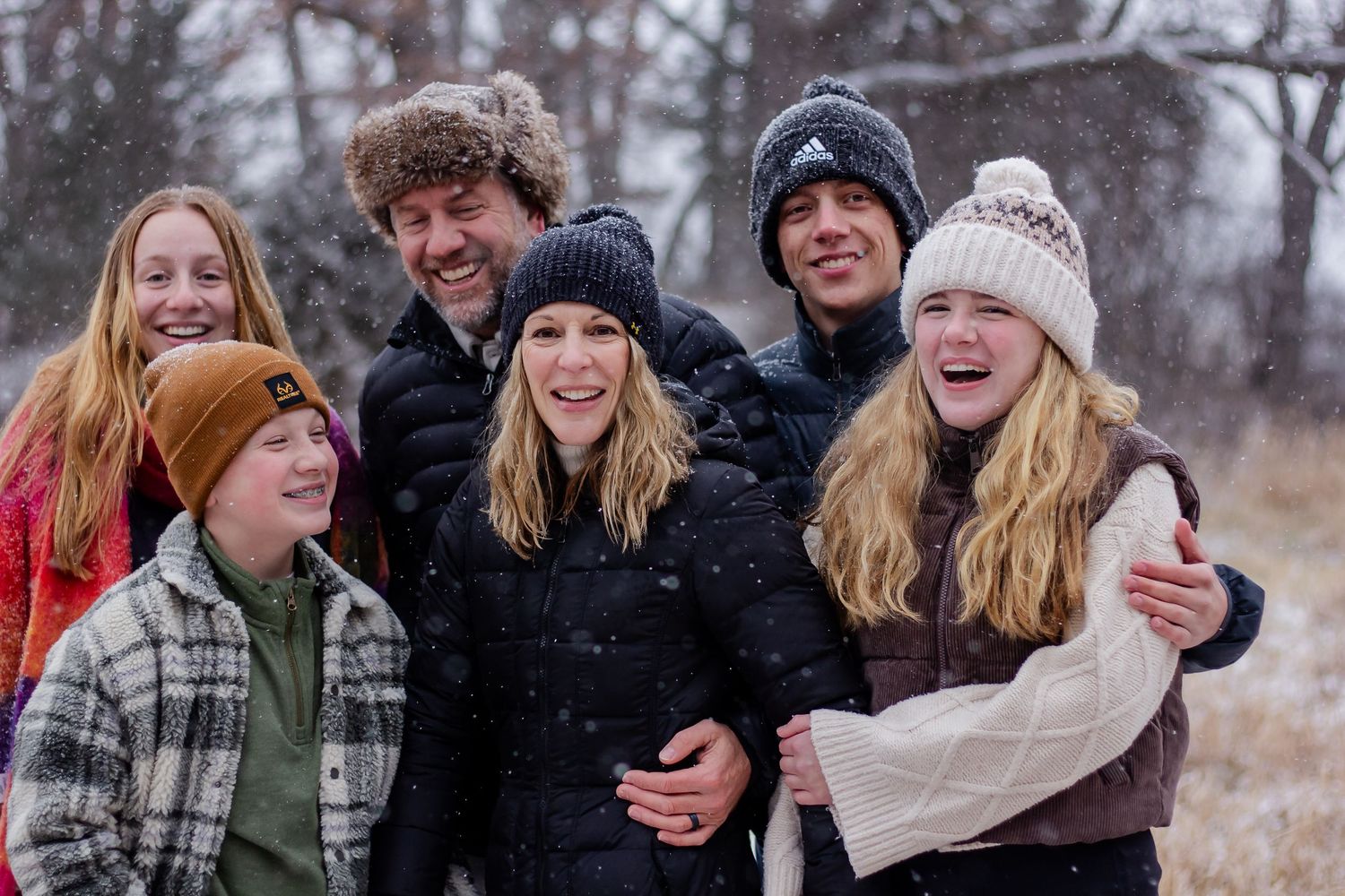 Group of friends bundled up in winter coats and hats laugh together outdoors during a snowy winter day in an Oconomowoc photo session