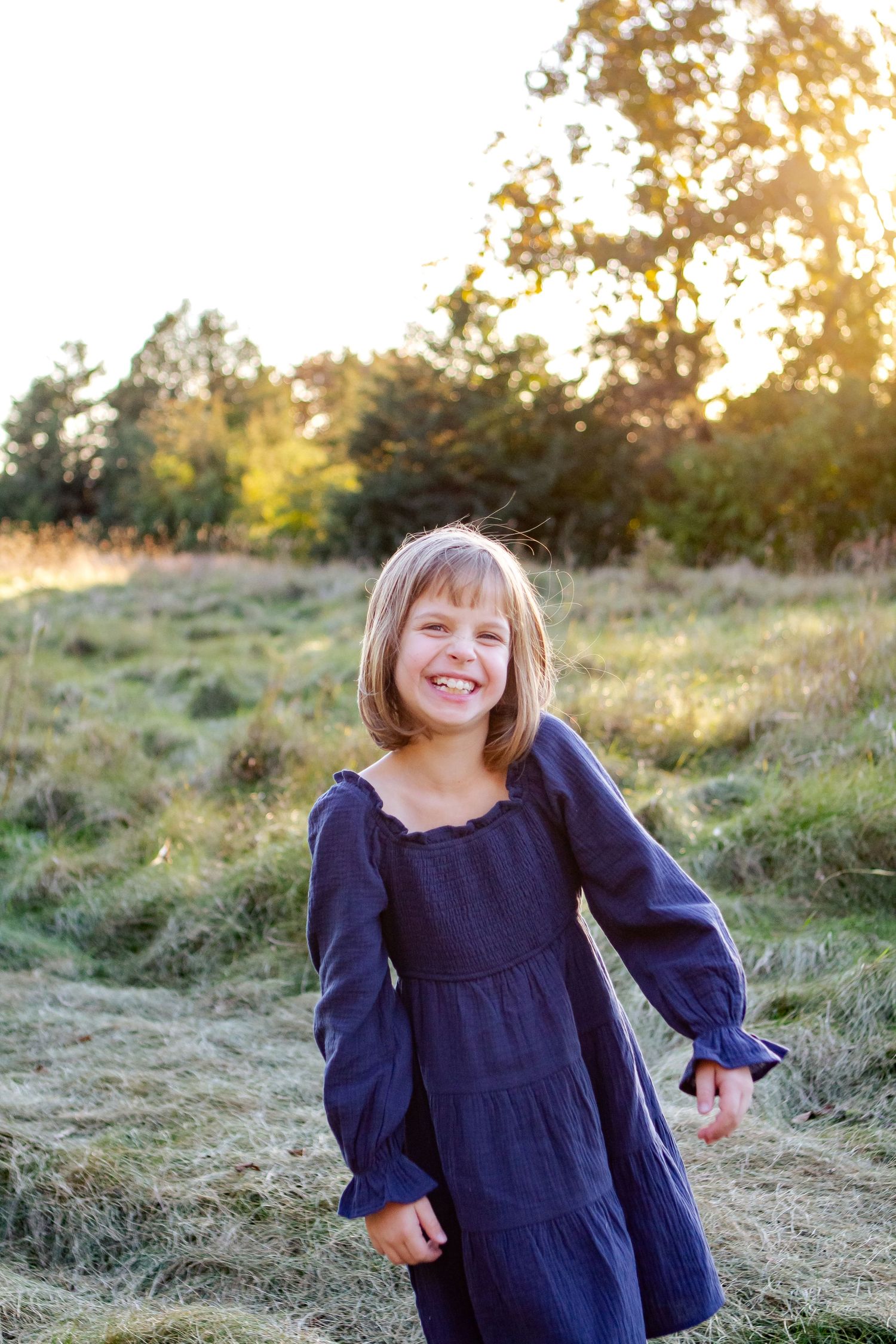 A child in a navy blue dress plays in a sunlit meadow during golden hour at an Oconomowoc family session