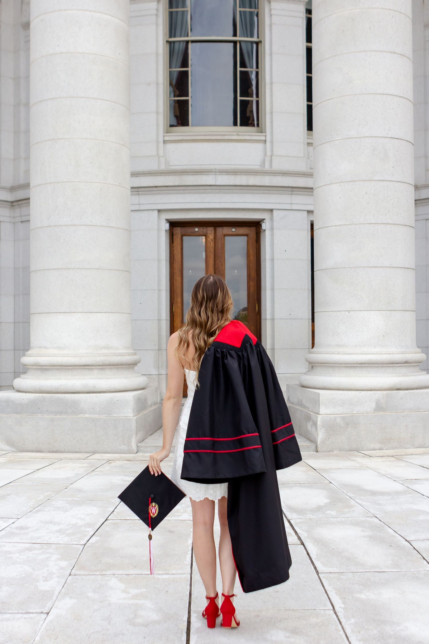 Academic regalia and red heels against white marble columns of a stately building.