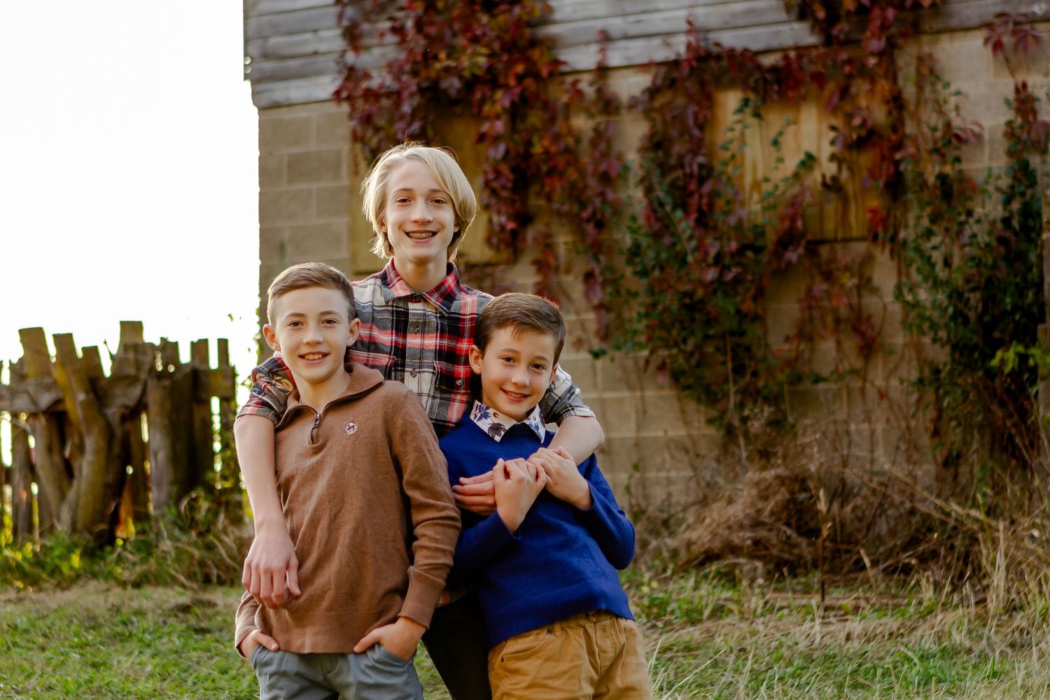Three children posing together in front of a rustic barn wall.