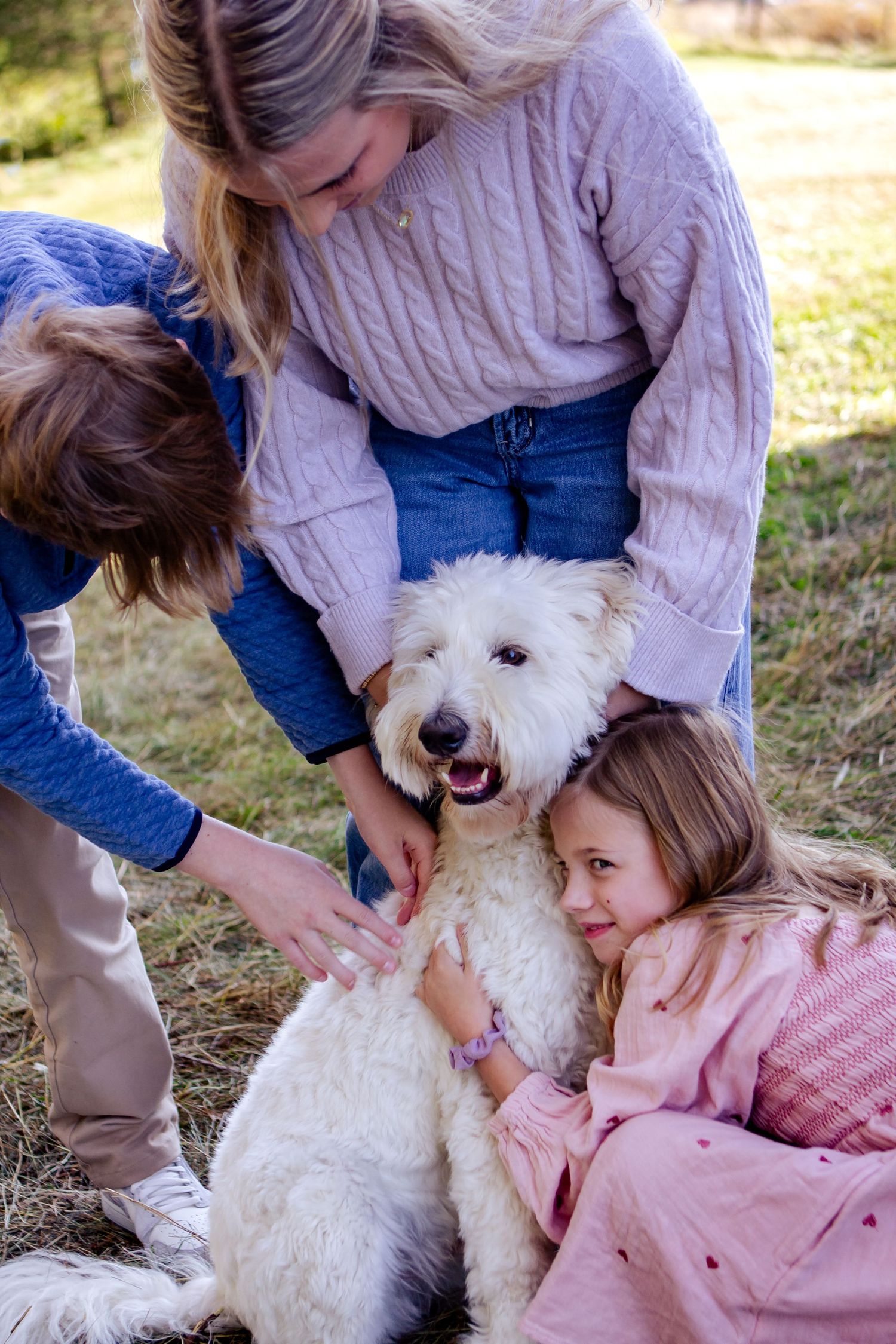 Heartwarming photos showing a white fluffy dog being hugged and petted by people in outdoor setting at a Lake Country Family session