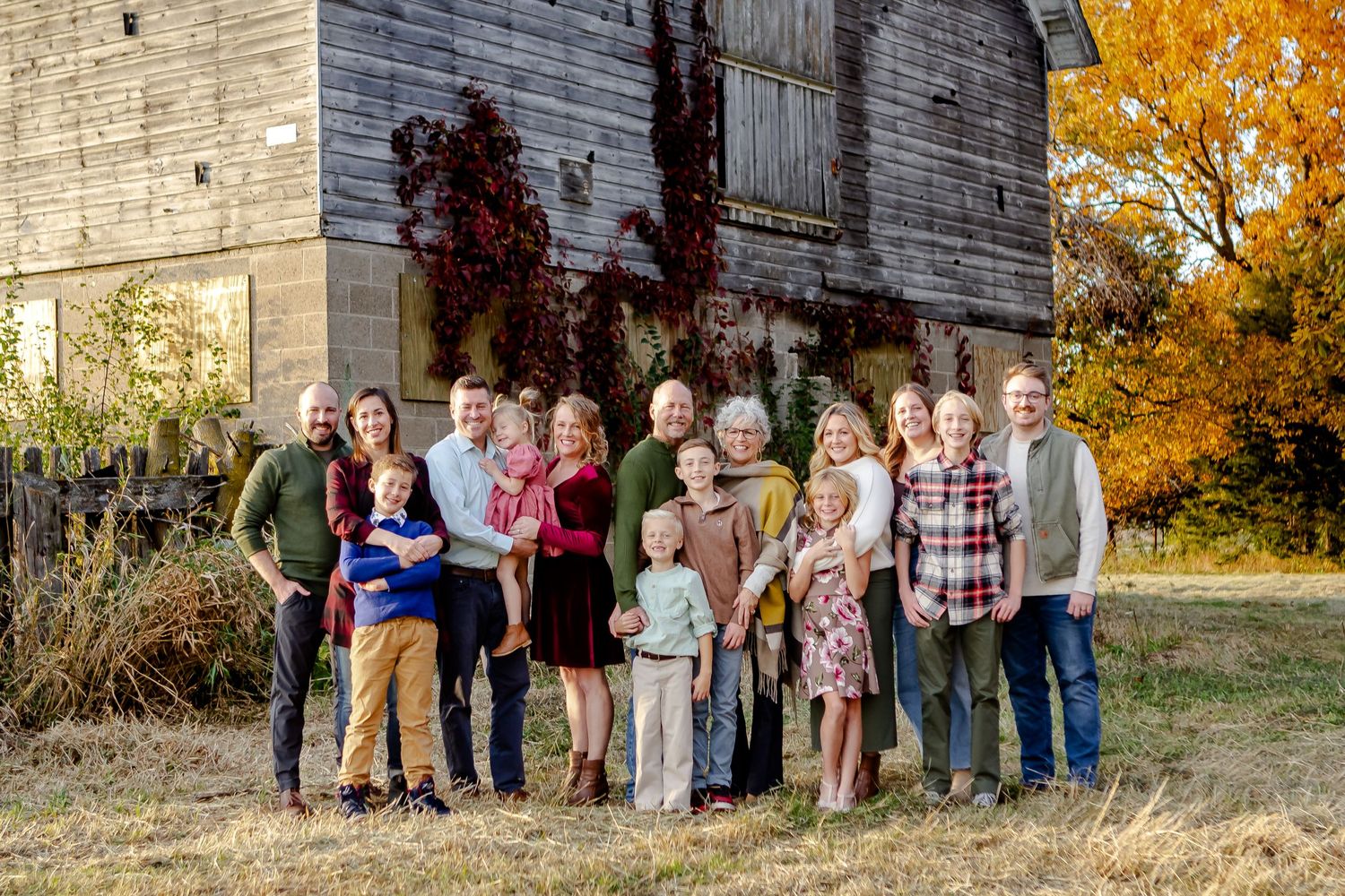 An extended family smiles outside of a barn during fall photo session in Oconomowoc
