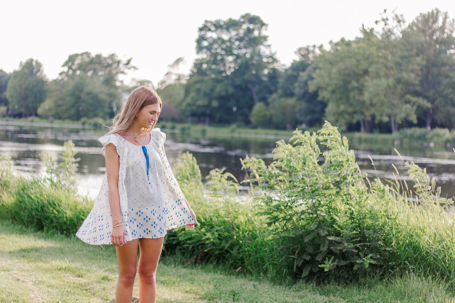 A waterside portrait in a white eyelet dress against a natural landscape.