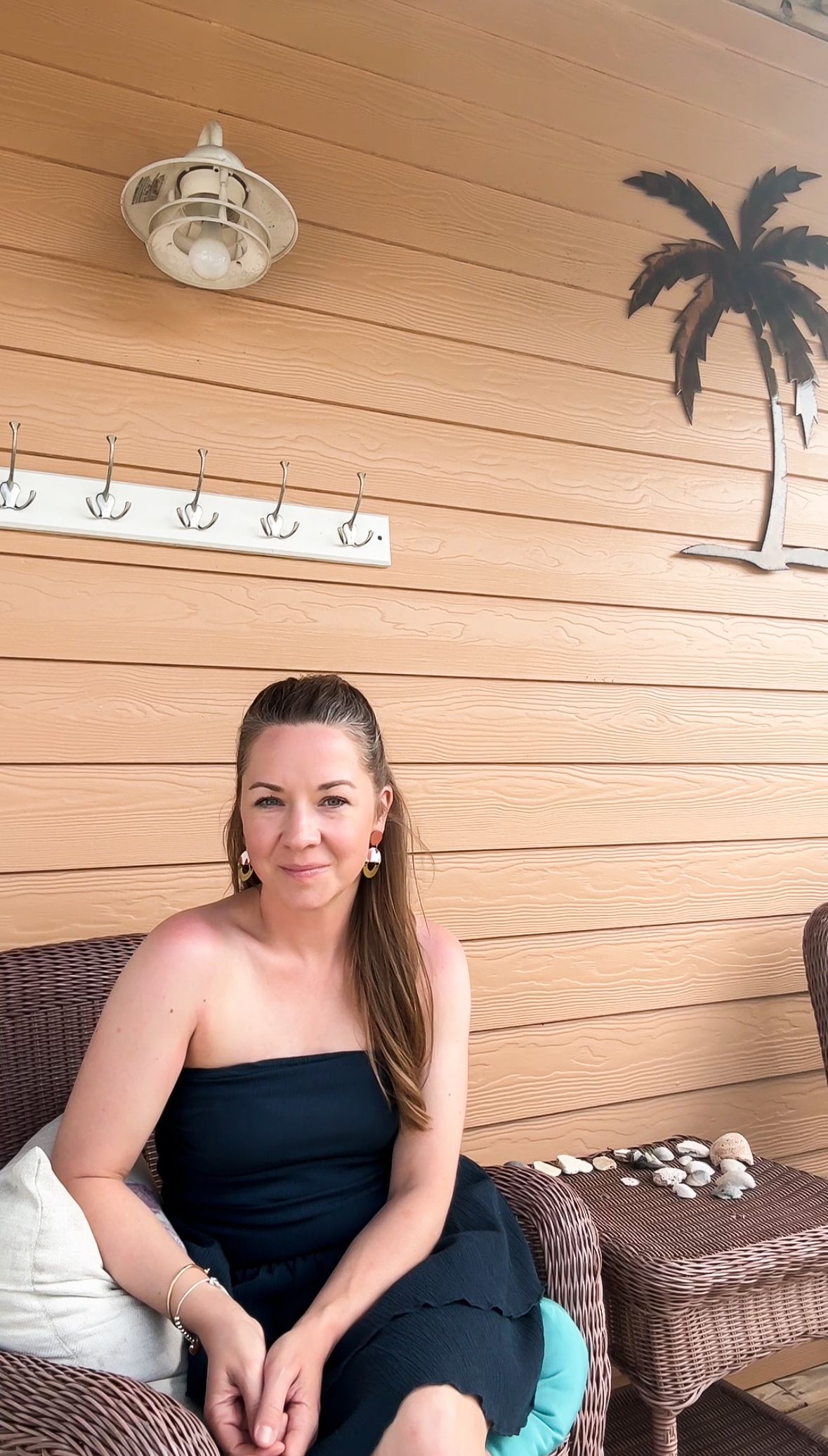Woman relaxing on wicker furniture against beige wall with coastal decor.