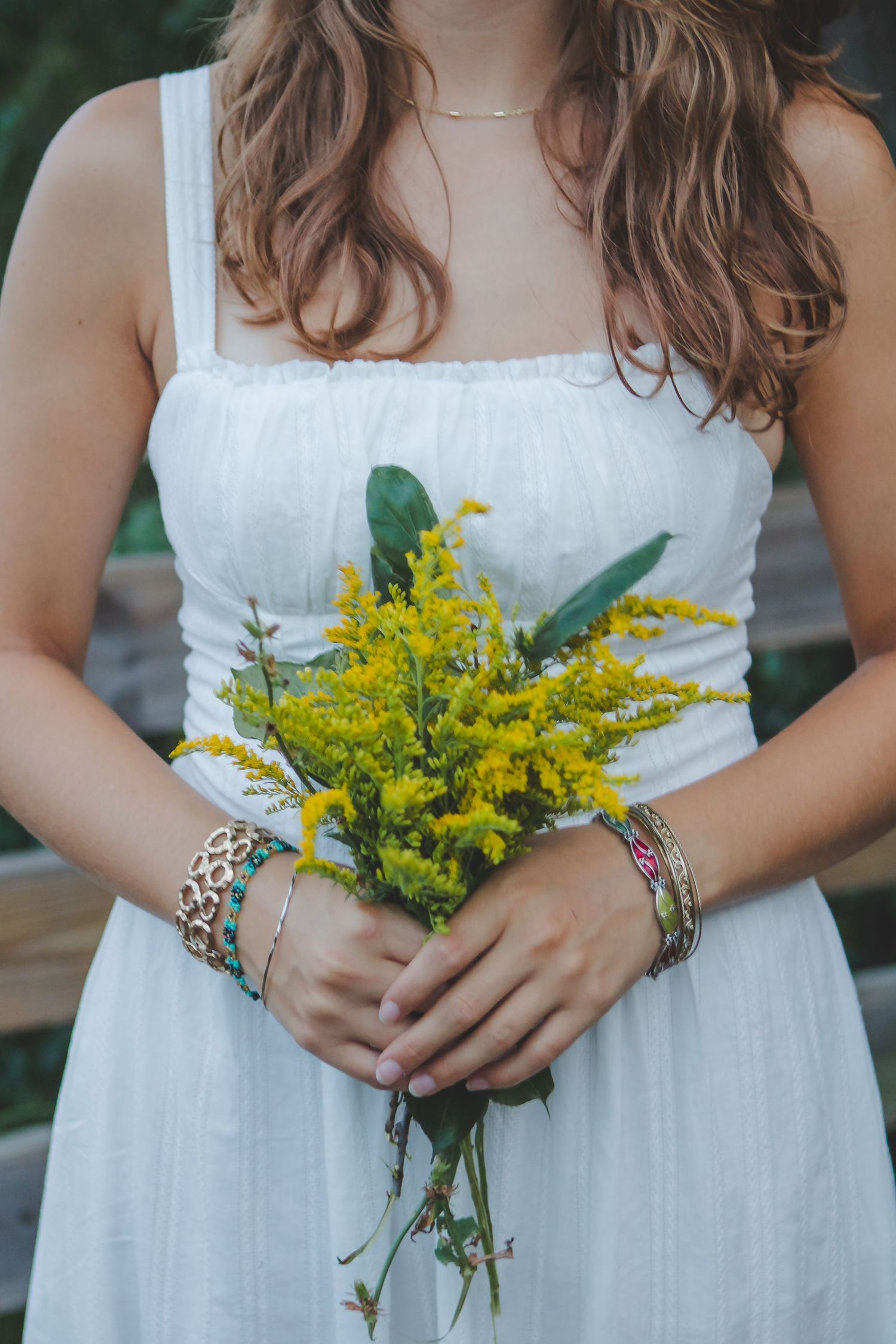 Hands hold a bouquet of bright yellow flowers against a white dress.