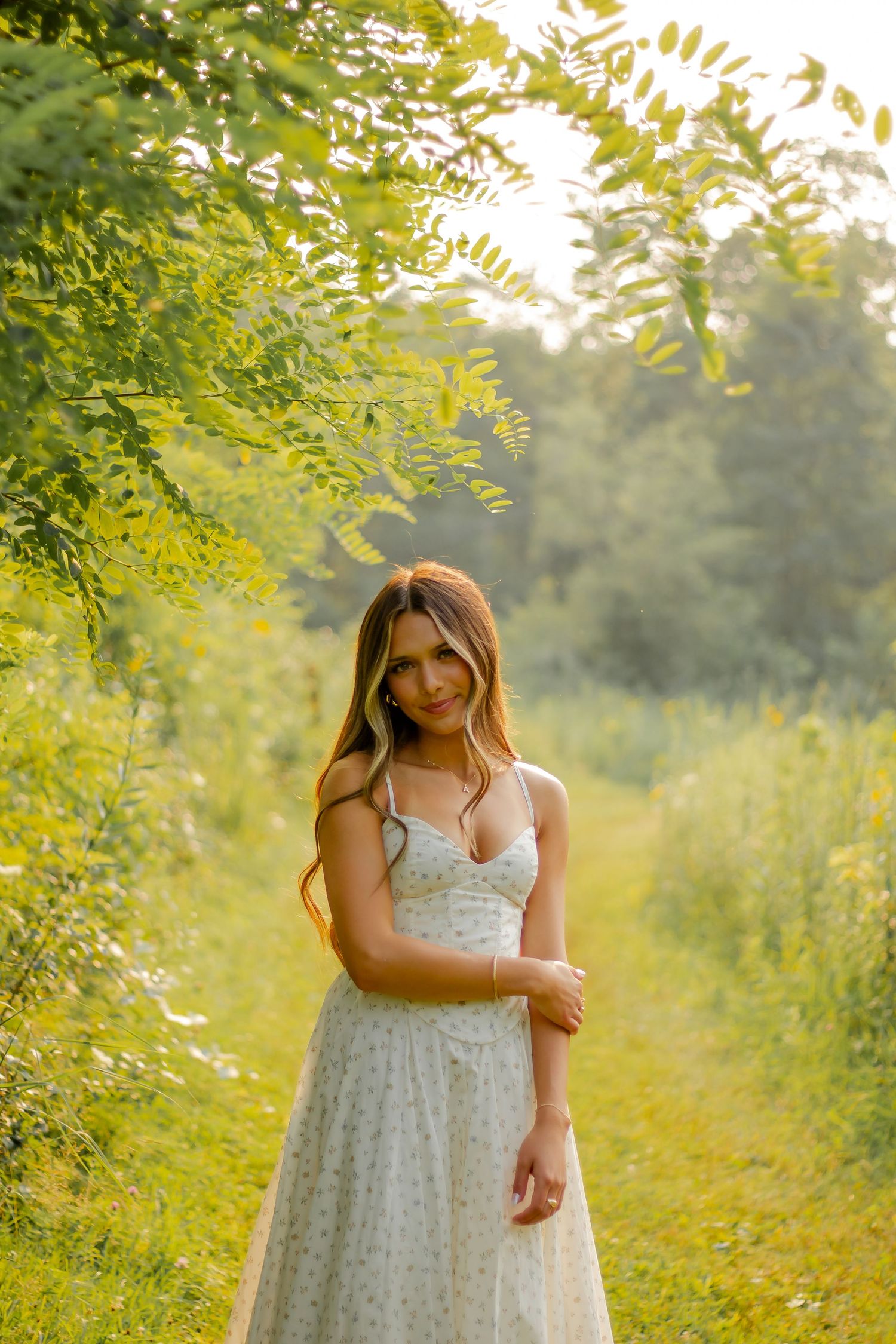 A floral white summer dress stands out against vibrant green foliage in warm sunlight.