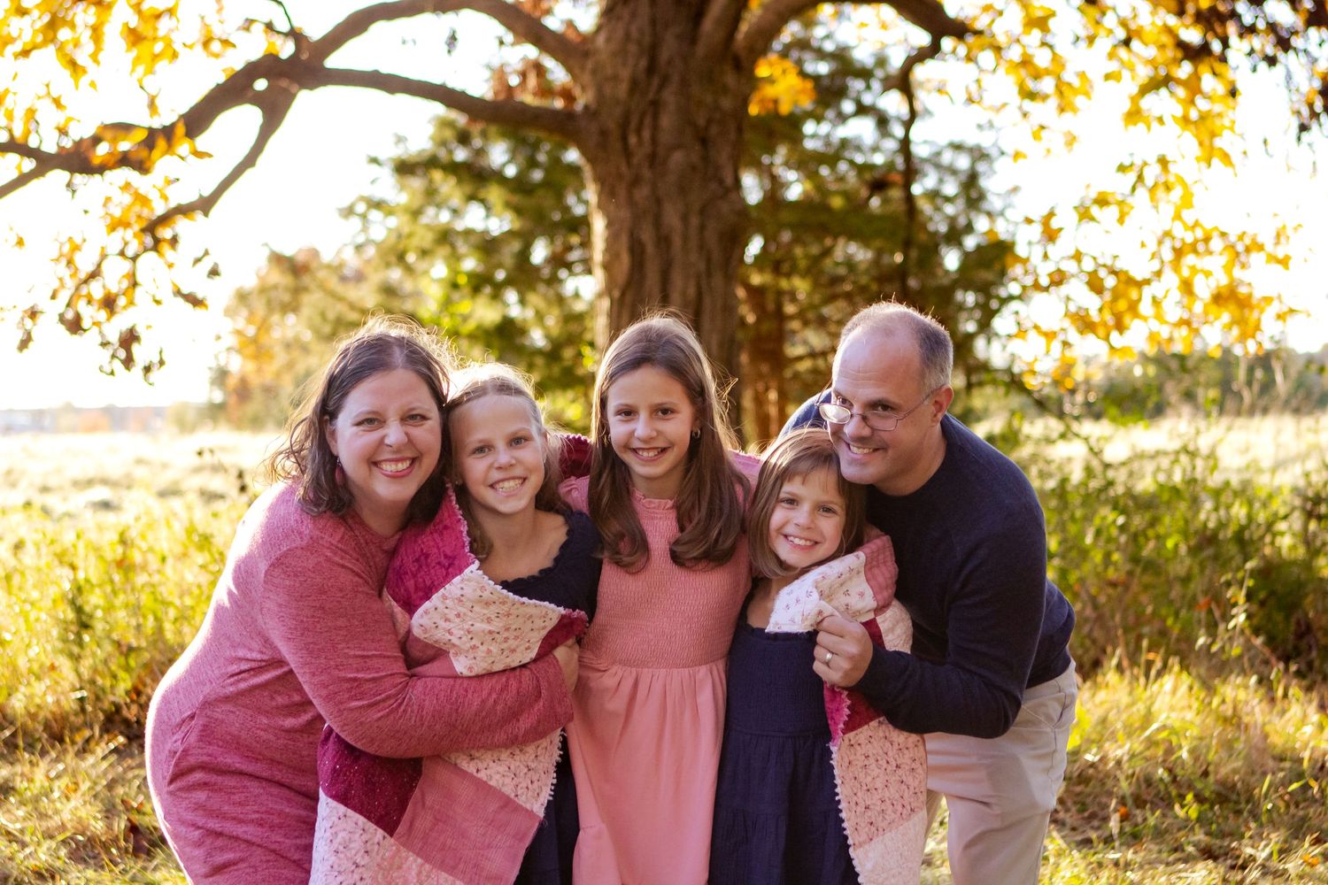 A group wearing coordinating pink and navy outfits poses together outdoors during golden hour in autumn at an Oconomowoc family session