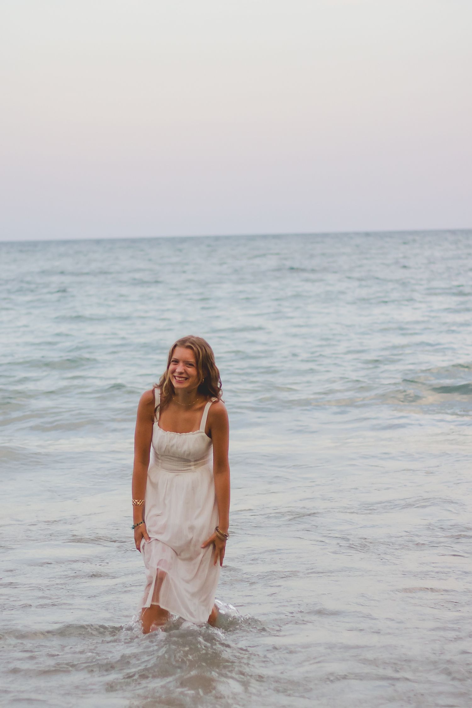 A carefree beach scene with someone wading through gentle ocean waves in a white dress.