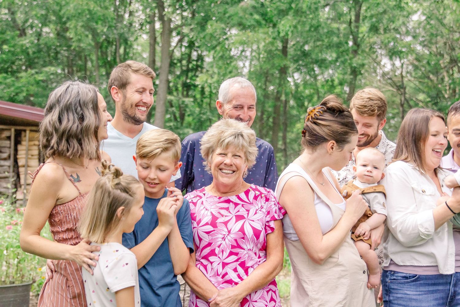 A multi-generational family gathering outdoors on a sunny day with trees in the background at Delafield home session