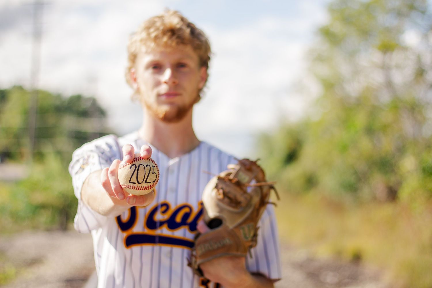 Baseball player in pinstriped uniform stands ready with mitt outdoors.