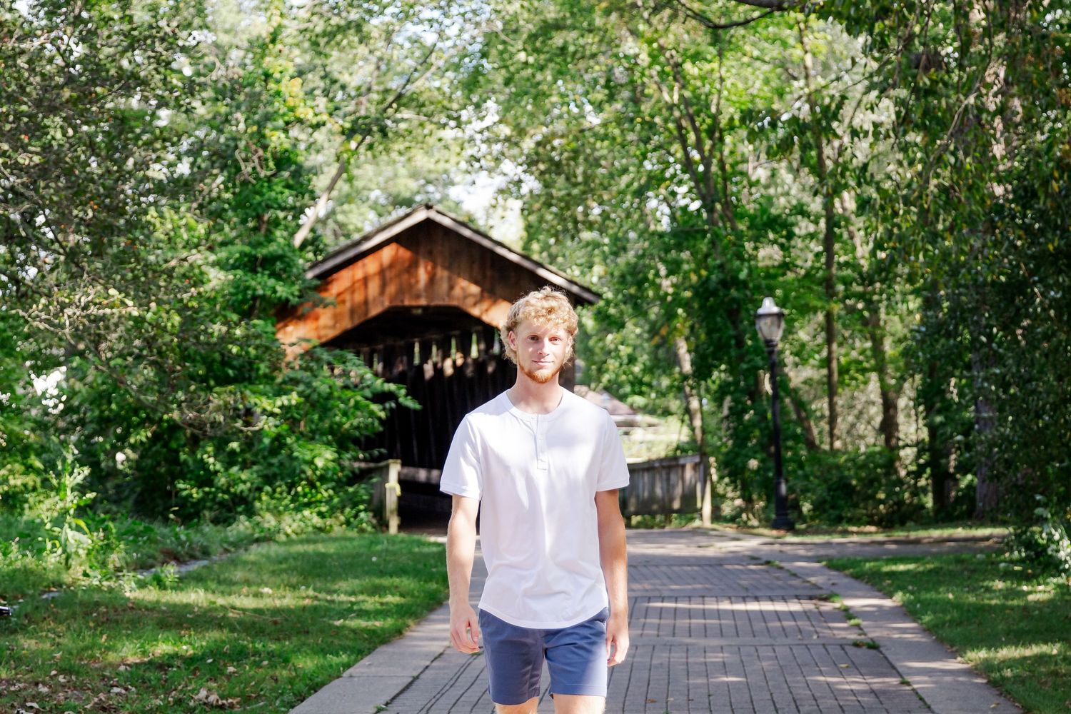 A person walks along a tree-lined path in a lush green park on a sunny day during a Michigan senior session