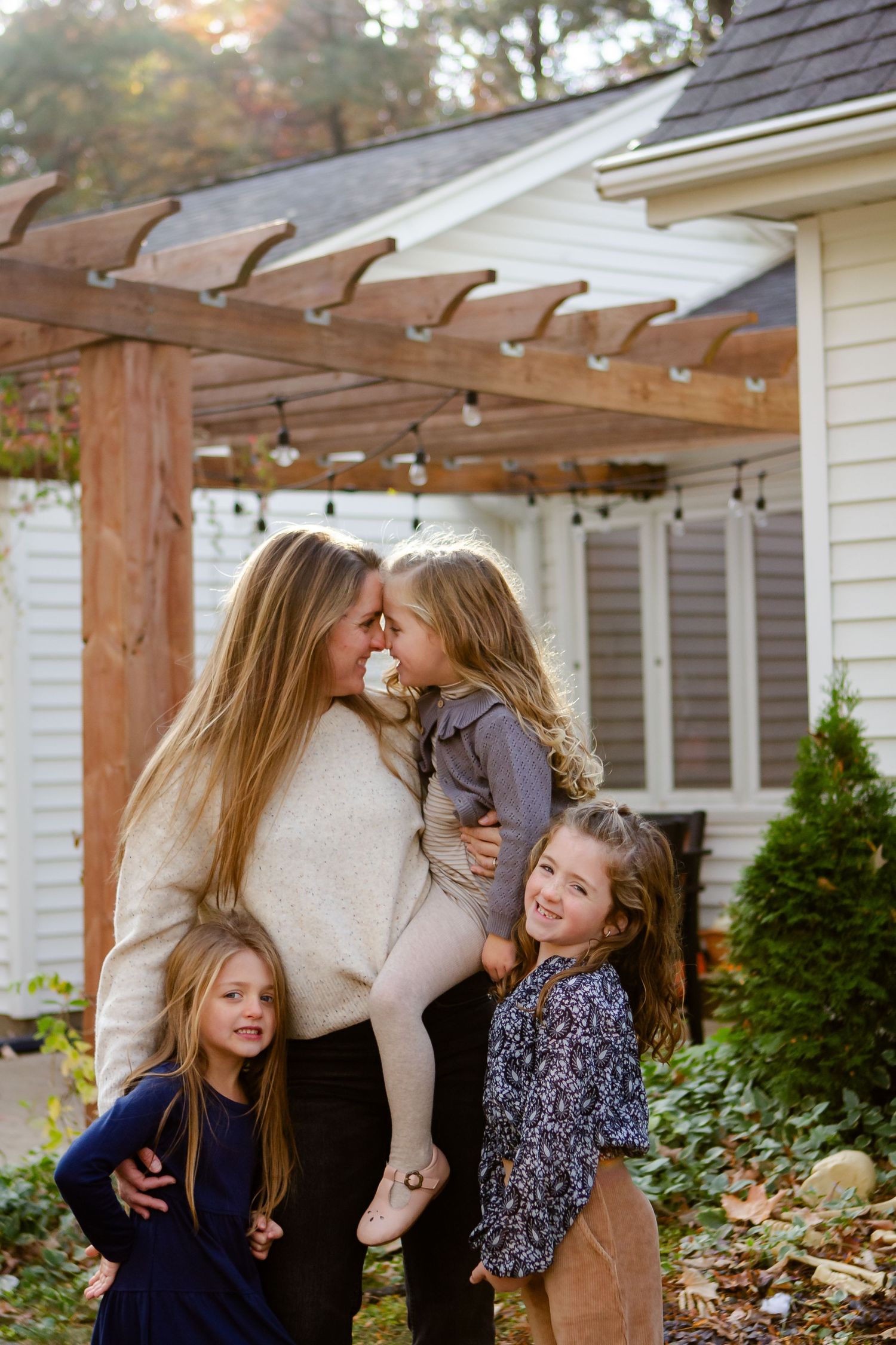 Family shares tender moments together under a wooden pergola during an outdoor photoshoot.