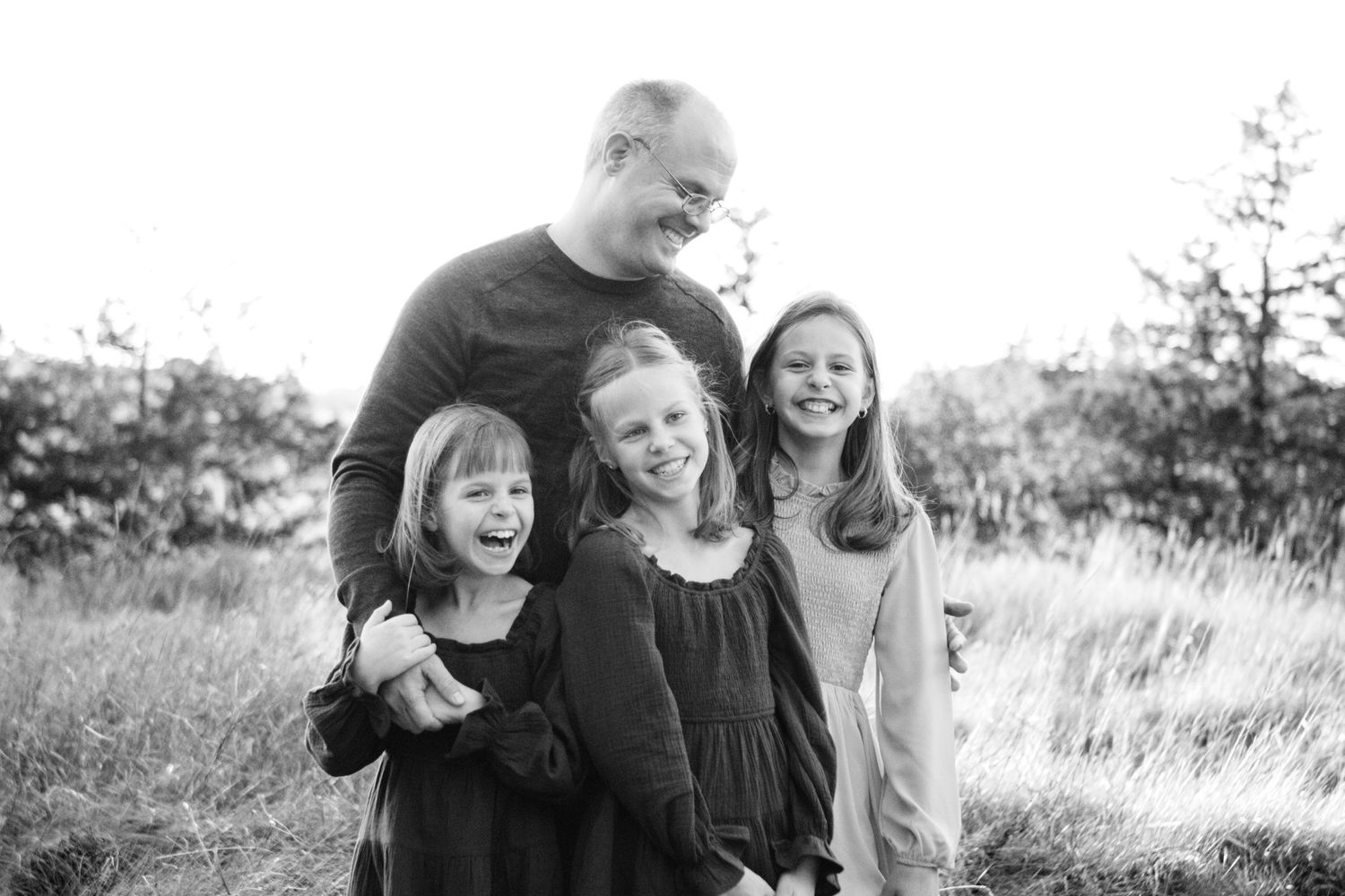 A black and white photo shows candid moments of people laughing and embracing outdoors in a natural setting at an Oconomowoc family session