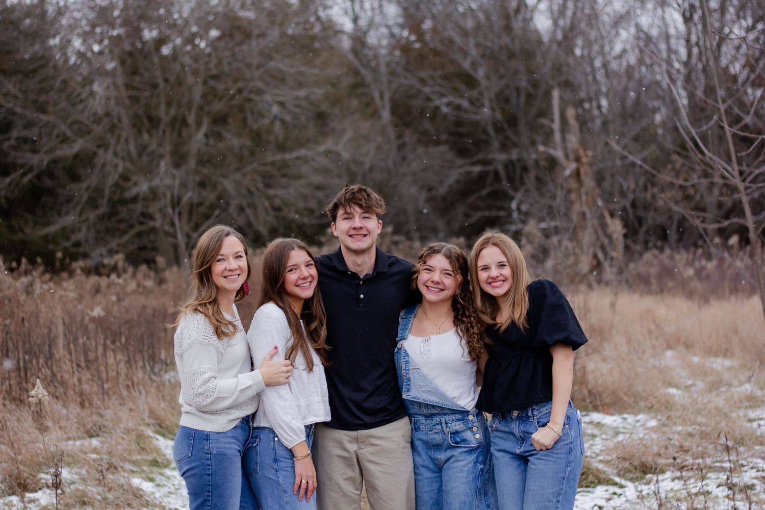 Group portrait of friends in denim and sweaters against snowy winter backdrop.