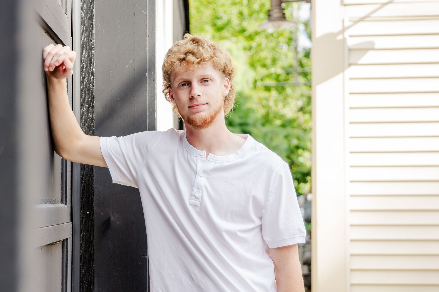 A relaxed pose leaning against a dark doorway in a white t-shirt.