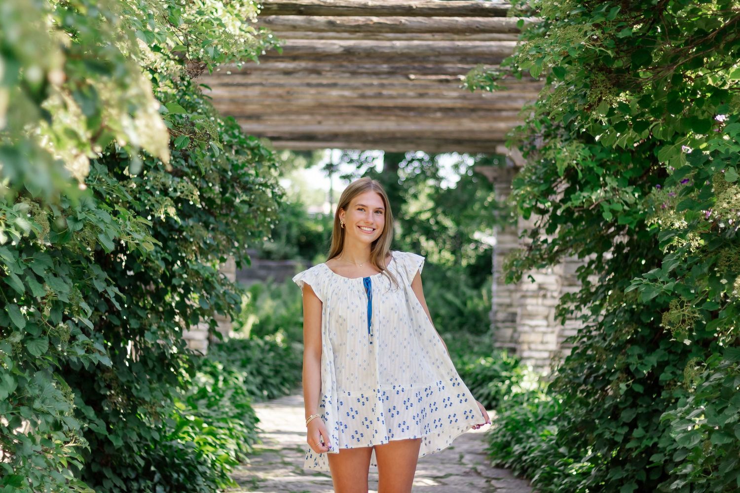 A breezy summer photo on a garden path wearing a white patterned dress.