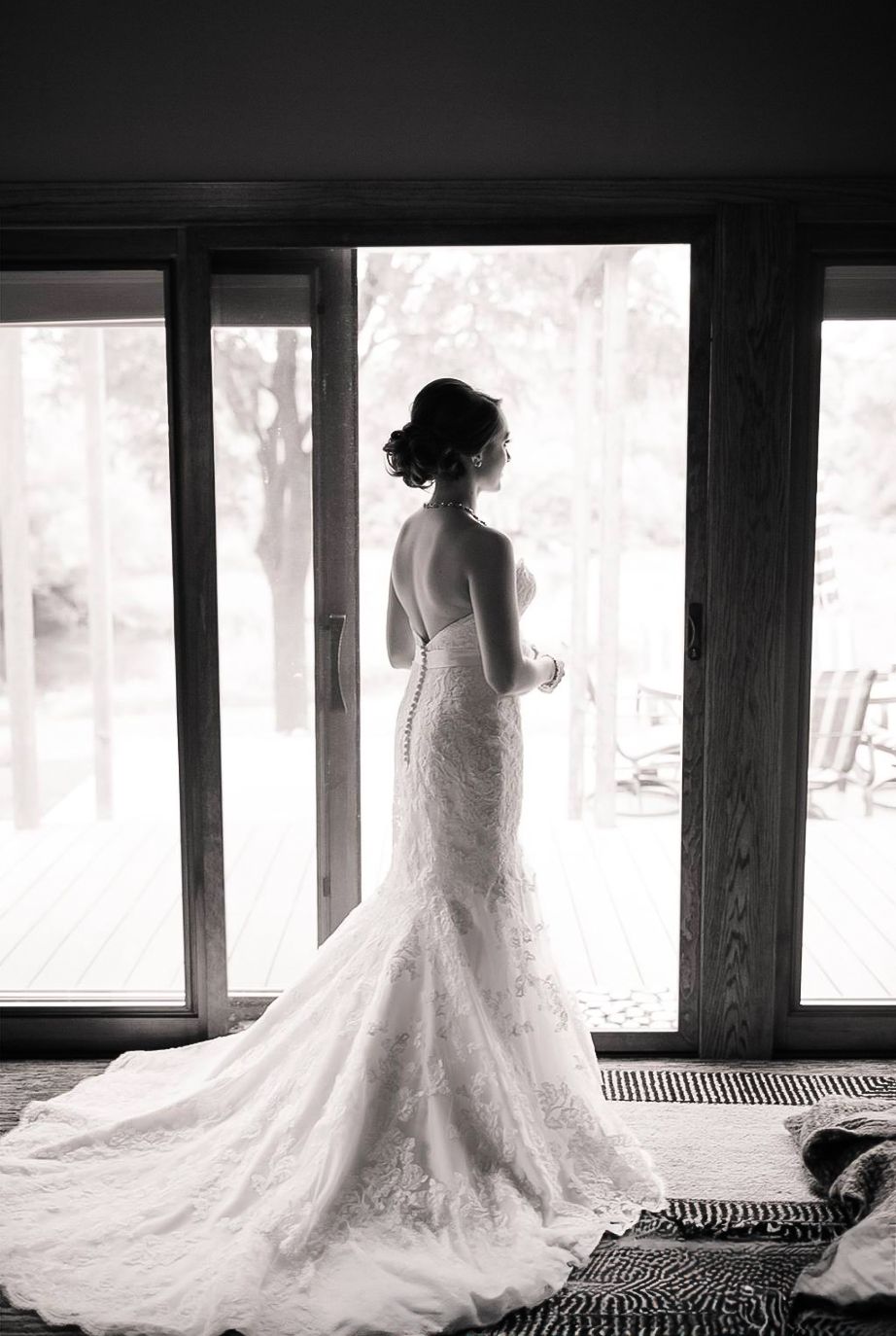 An elegant lace wedding dress with a long train photographed in silhouette against bright windows.
